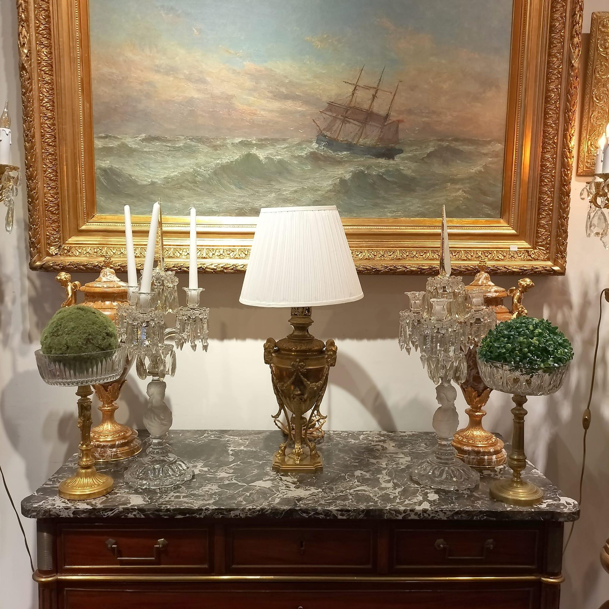 Lampe de table en bronze doré du XIXe siècle, ornée de motifs de têtes de bélier et de motifs floraux. 

La base a une forme carrée avec une plateforme surélevée, soutenue par des  Quatre pieds courbés et décorés de façon complexe de rinceaux, se