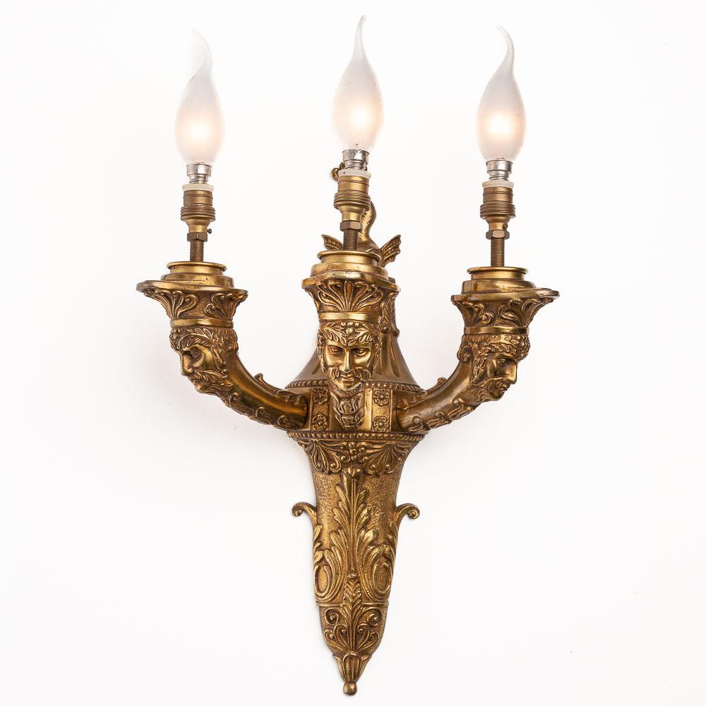 A pair of scones in gilt bronze. Each piece holds three arms of lights. The front part represents an old man's head, the back part is decorated with a griffin.
 