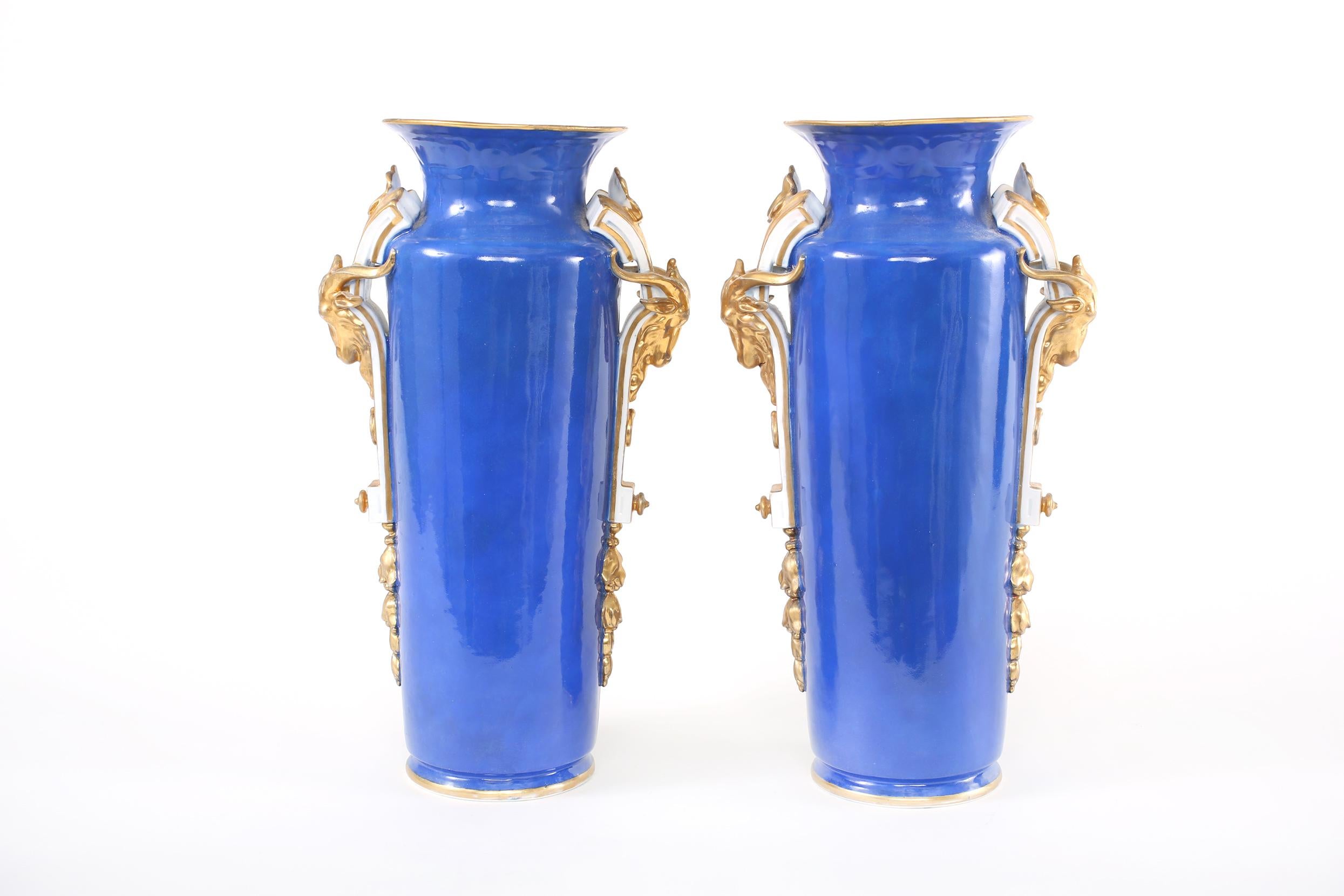 Mid 19th century pair gilt porcelain decorative vases with gilt gold handles and exterior painted scene details. Each vase / urn is in great antique condition. Minor wear consistent with age / use. Each piece stands about 19 inches tall x 11 inches