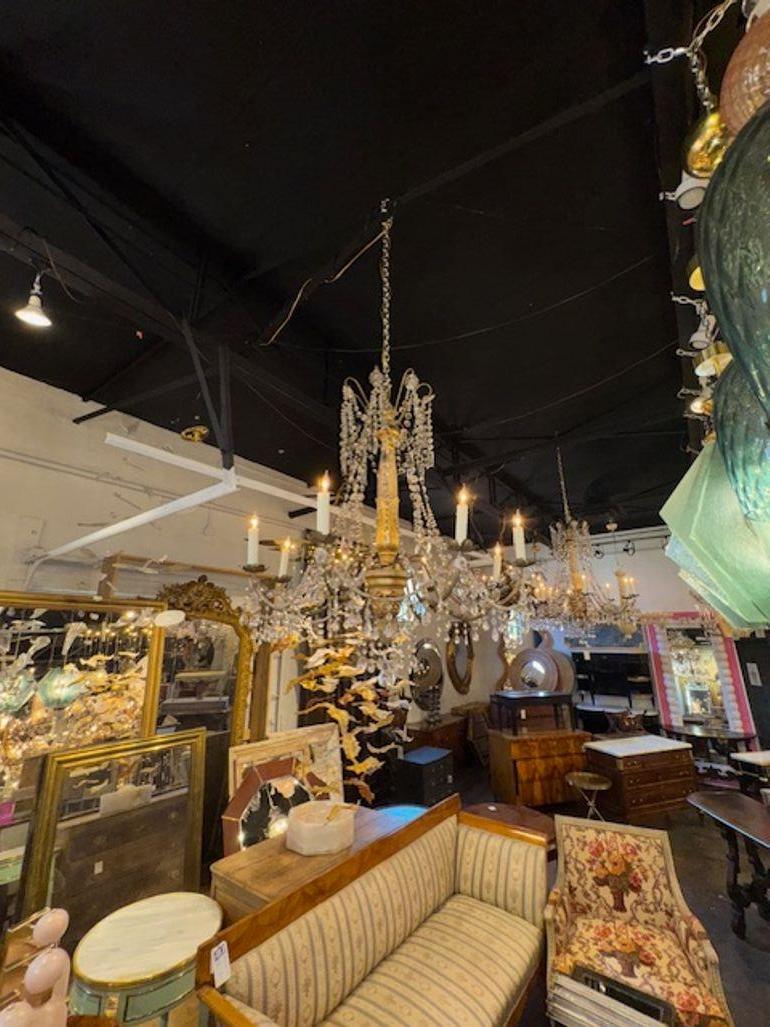 Ce lustre en bois doré, perles et cristaux du 19e siècle, originaire de Gênes, présente un design élégant et classique avec des détails complexes. Le lustre est orné de perles et de cristaux, ajoutant une touche d'élégance et de sophistication à