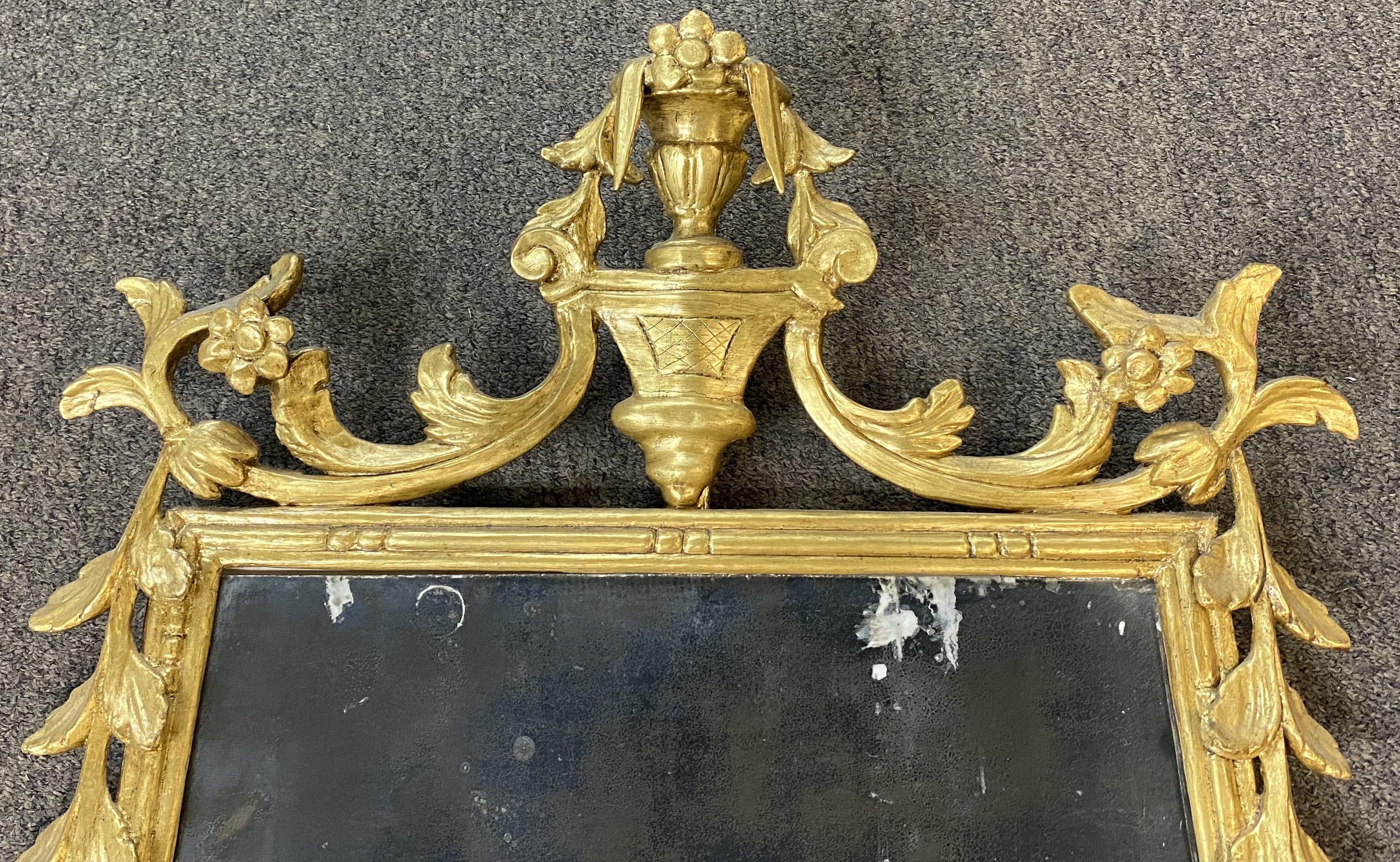 Un beau miroir rococo en bois doré sculpté, avec une crête en forme d'urne entourée d'une bordure sculptée de rinceaux, et qui semble avoir conservé sa vitre d'origine, avec quelques taches de peinture. Probablement d'origine italienne, datant du