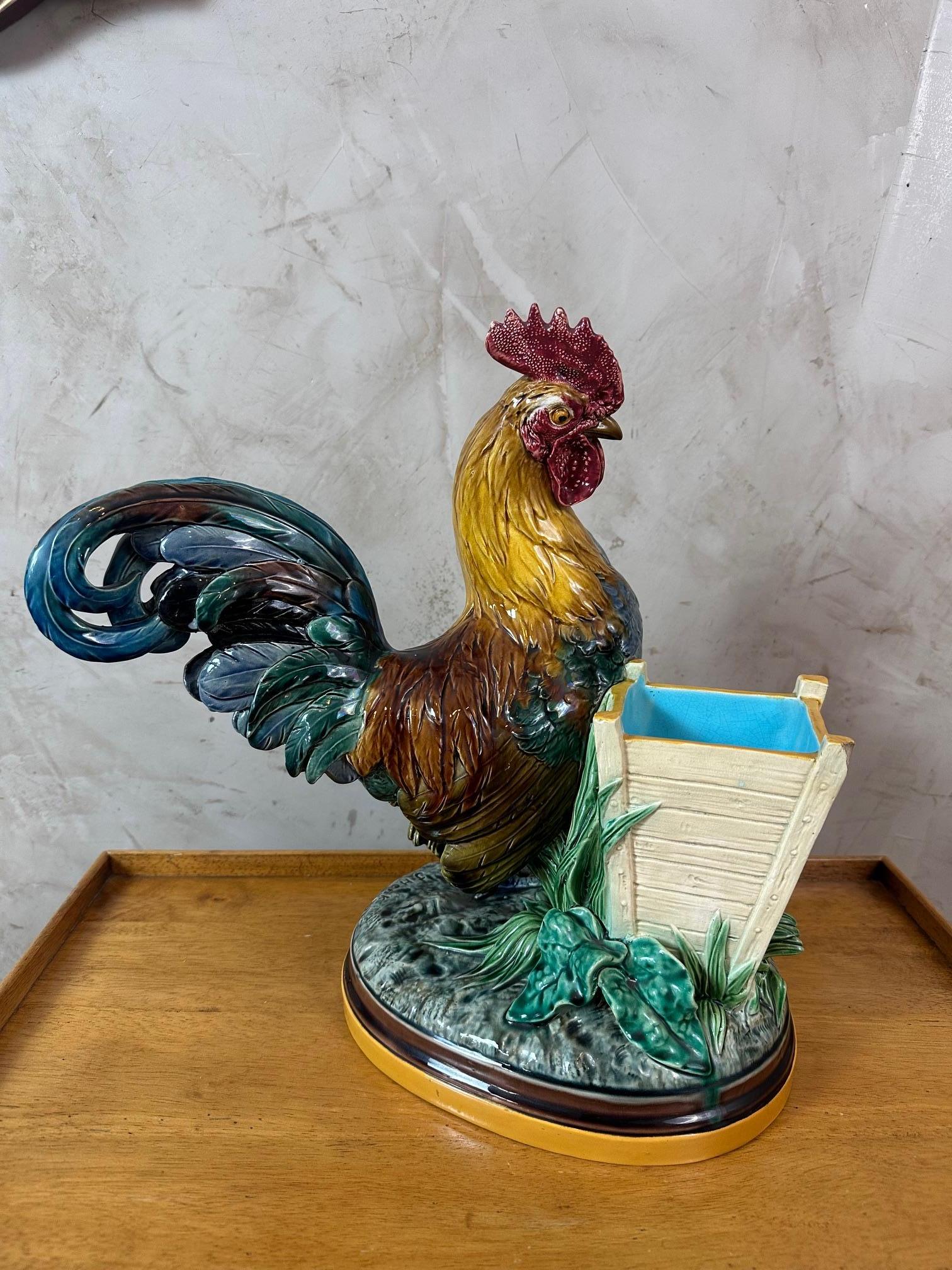 Il s'agit d'un magnifique coq debout en majolique émaillée. À côté se trouve un grand panier ouvert servant de jardinière, sur une base ovale avec des feuilles appliquées. Signature John Henk sur la base. Datant de la fin du 19e siècle. Marque