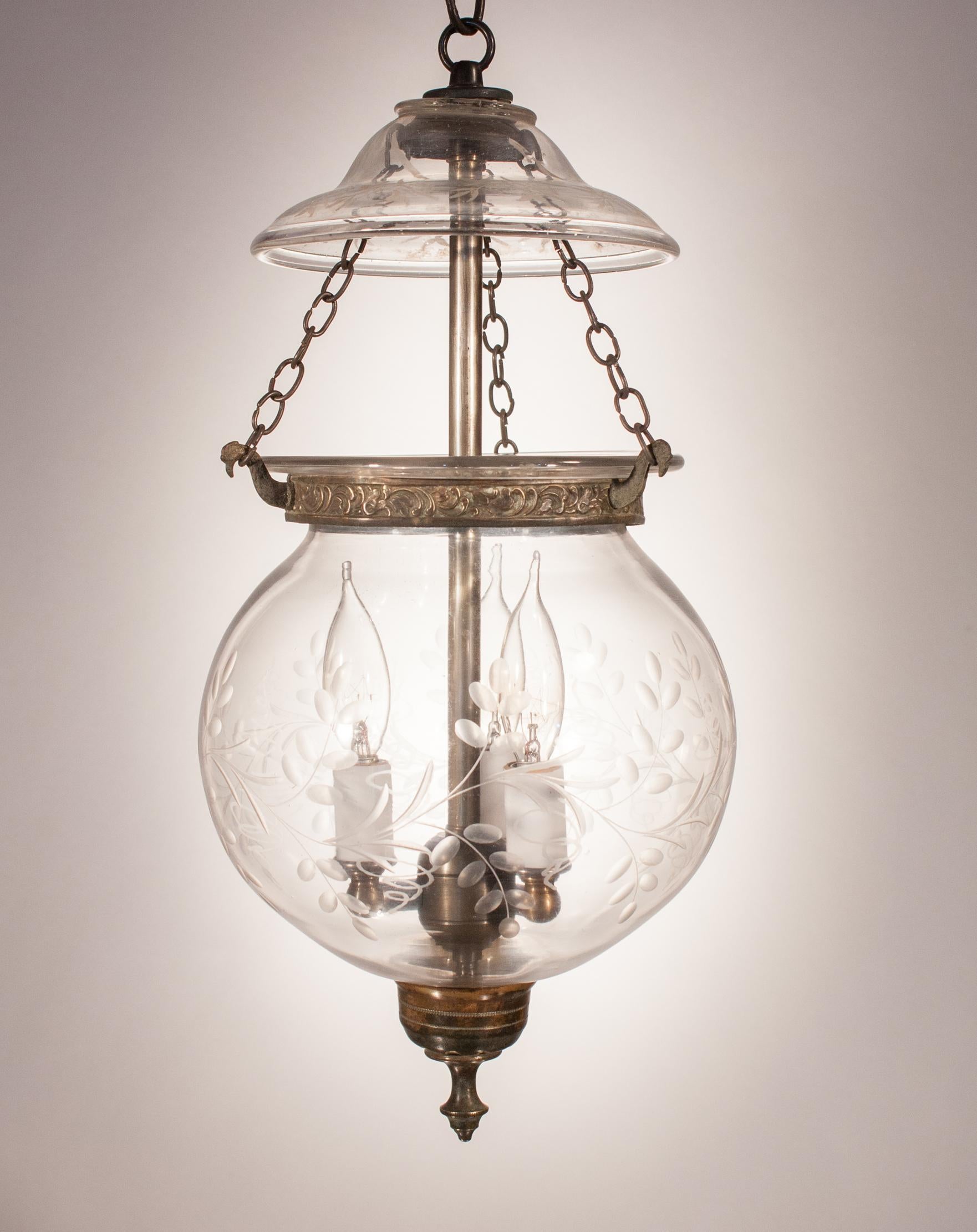 A hand blown glass globe bell jar lantern, circa 1870, with lovely form and a fluidly etched vine motif. The lantern features its original, embossed brass band and finial, which is difficult to find in a globe this old. Shown here with a decorated
