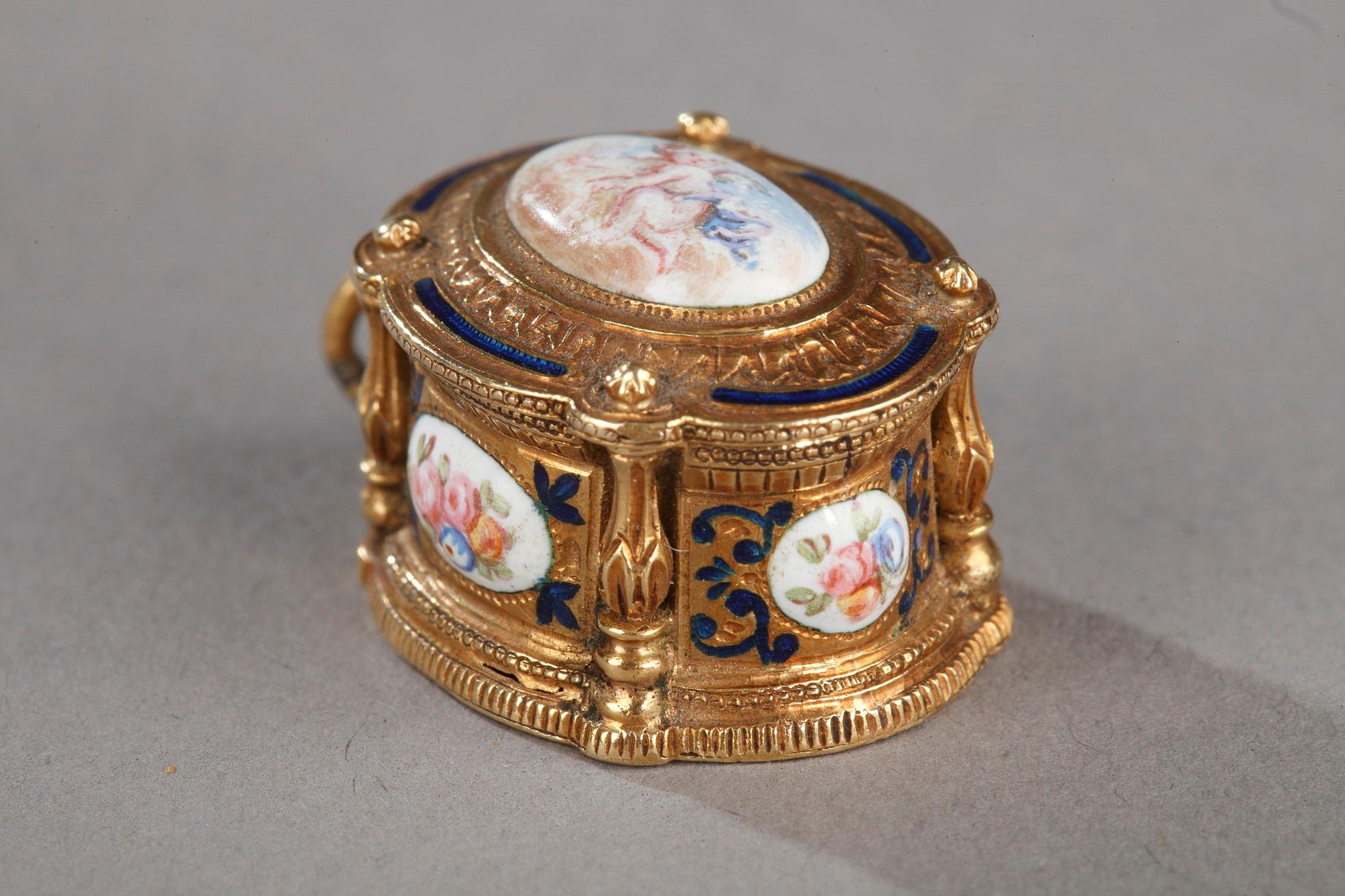Small little box of oval shape mounted as a pendant. The hinged lid and the side are adorned with enamelled medallions representing putti or floral arrangements. The medallions are framed by translucent blue enamelled motifs and a fine engraving. On