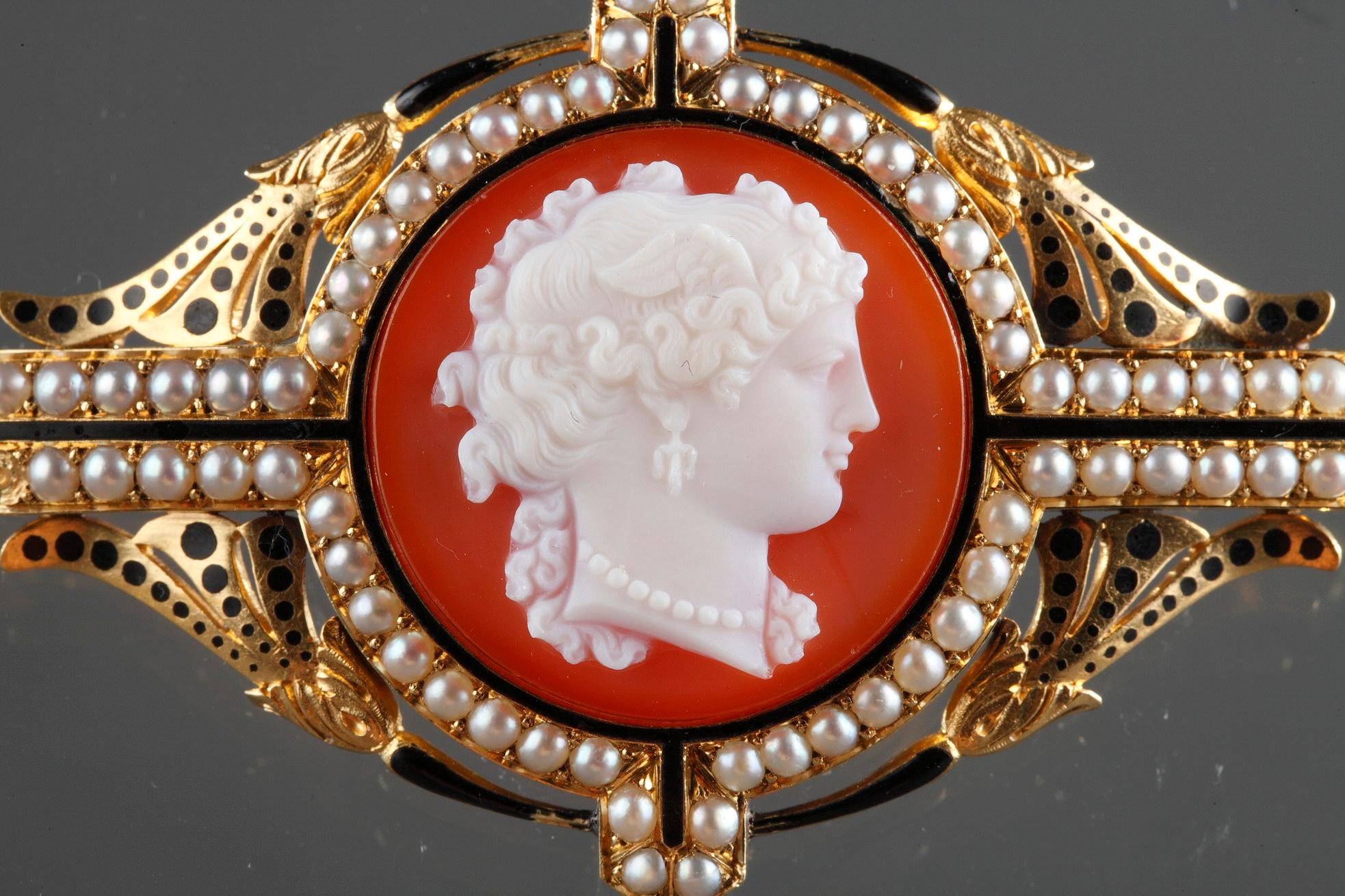 A gold-mounted agate cameo brooch depicting the bust of a young woman wearing a pearl necklace. Openwork gold mounts decorated with pearls and black enamel floral motives. Ancient clasp.
French hallmark for gold : eagle's head (tête