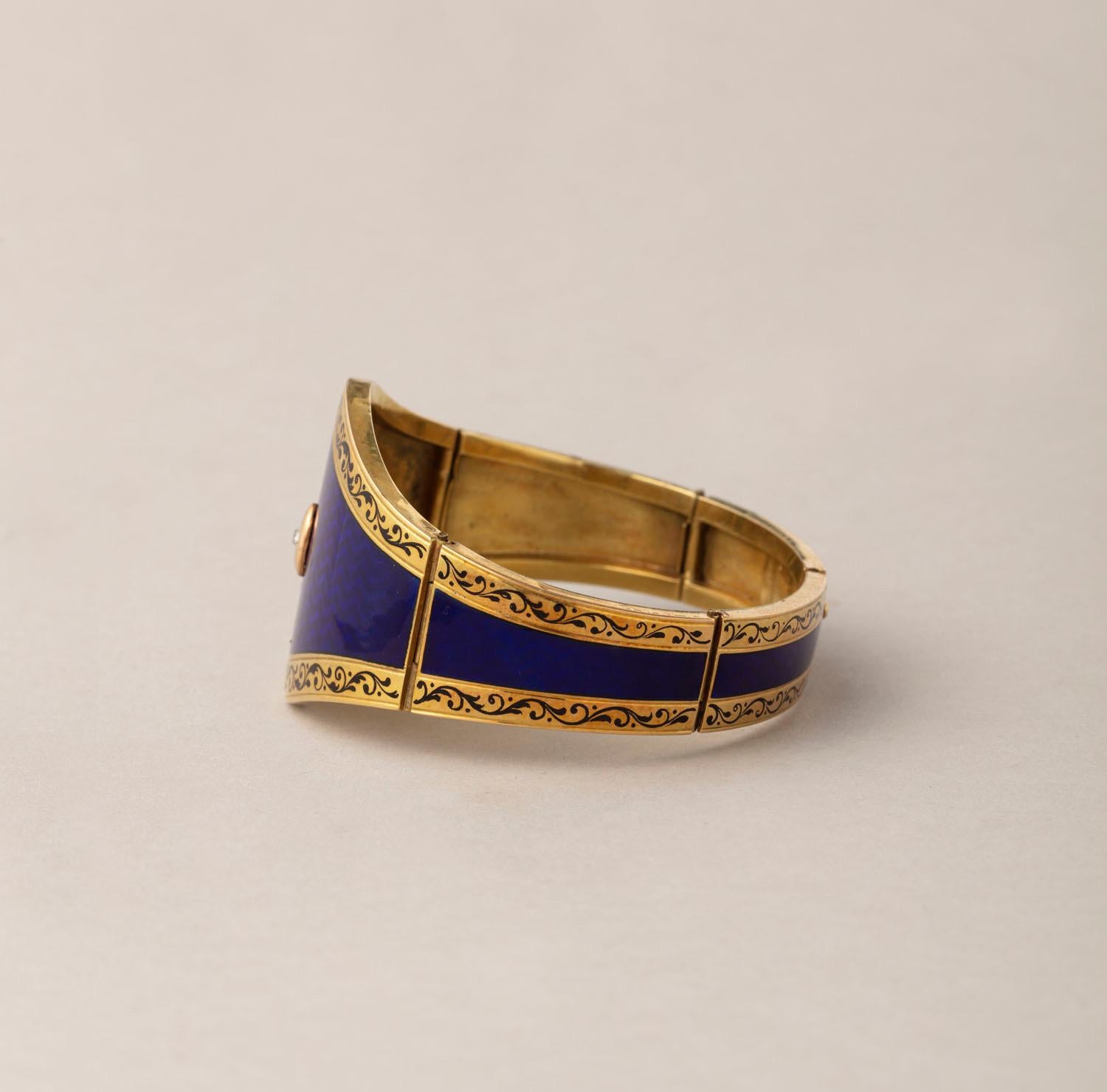 A 14 carat gold bangle decorated all over with perfect night blue translucent enamel over a wave like guilloche, wider at the front with a diamond detail, narrowing at the back, on each side is a border with black enamel scrolls, the bangle opens