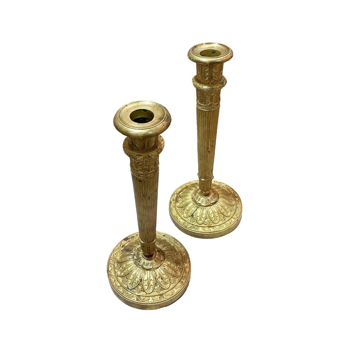 A gold, antique French pair of candle holders with loose candle cuffs, made of hand crafted gilded bronze, in good condition. The detailed candlesticks have downwardly tapering, fluted shafts, supported by a round footplate. The base is