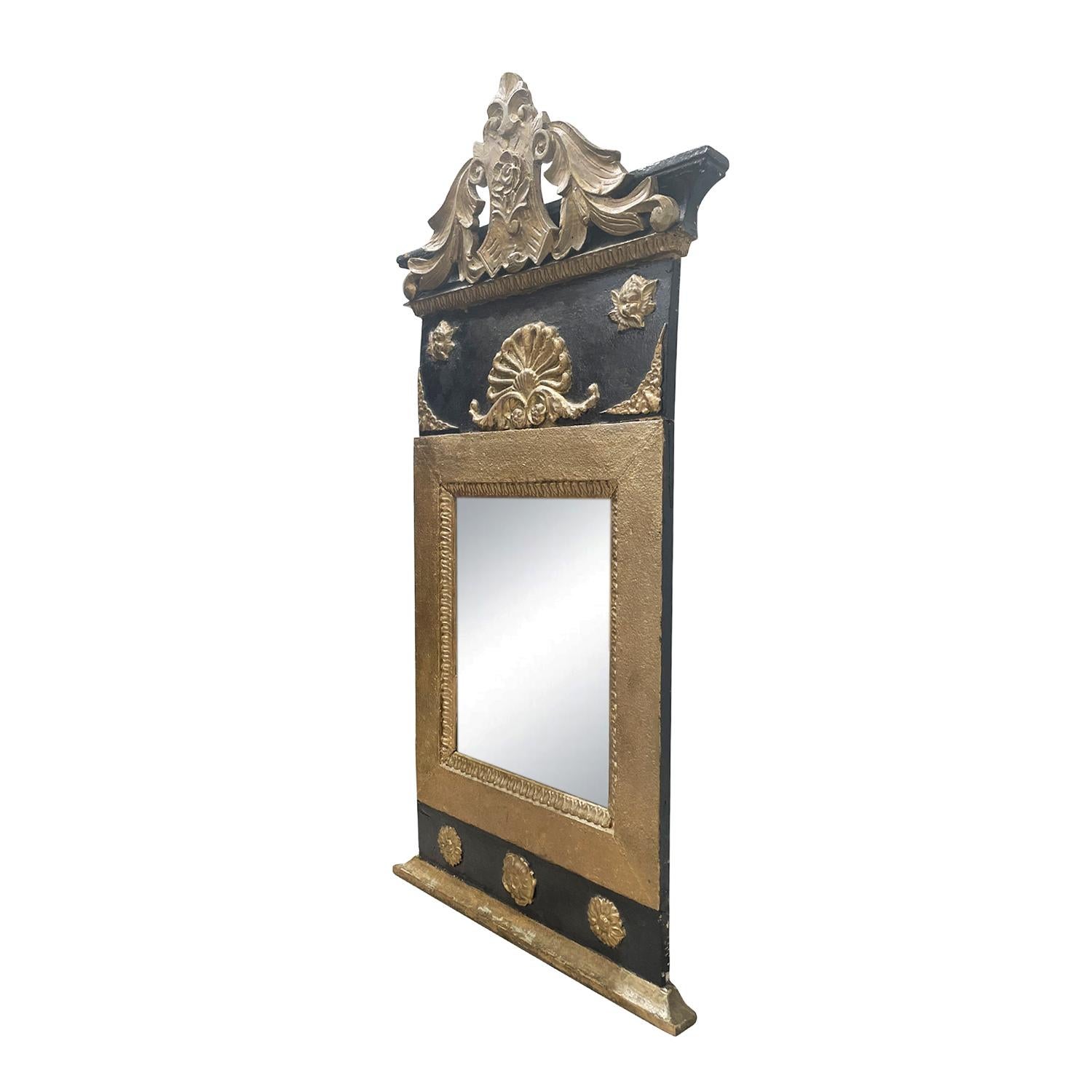 A black-gold, antique French wall mirror made of hand crafted gilded Pinewood with its original mirrored glass, in good condition. The particularized carved Parisian mirror is enhanced by detailed flower wood carvings and fittings. The décor piece