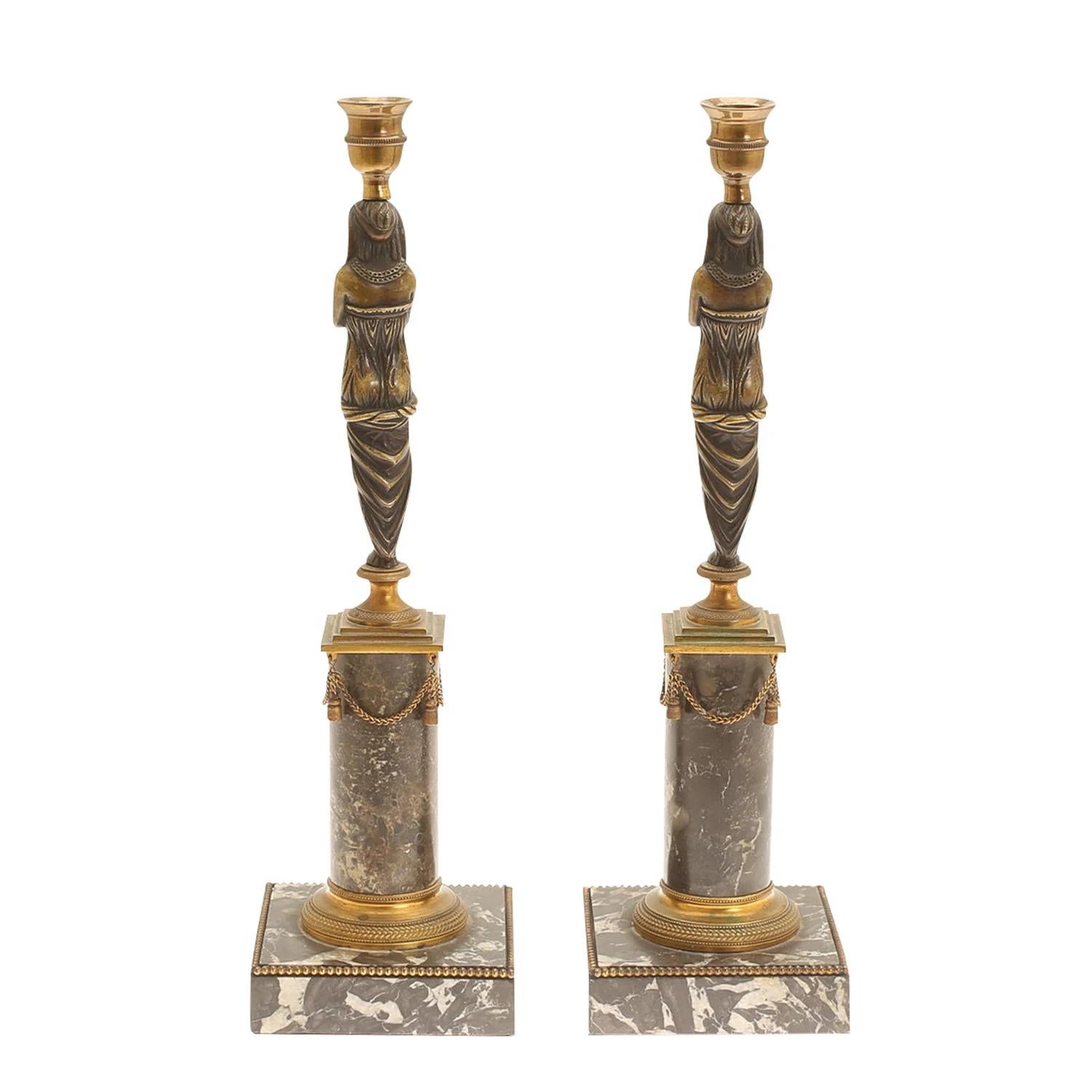 A gold, antique French pair of Egyptian women figure candle holders made of handcrafted marble and patinated bronze, in good condition. The candle sticks are resting on an urn-shaped base. The particularized Parisian décor pieces represent the First