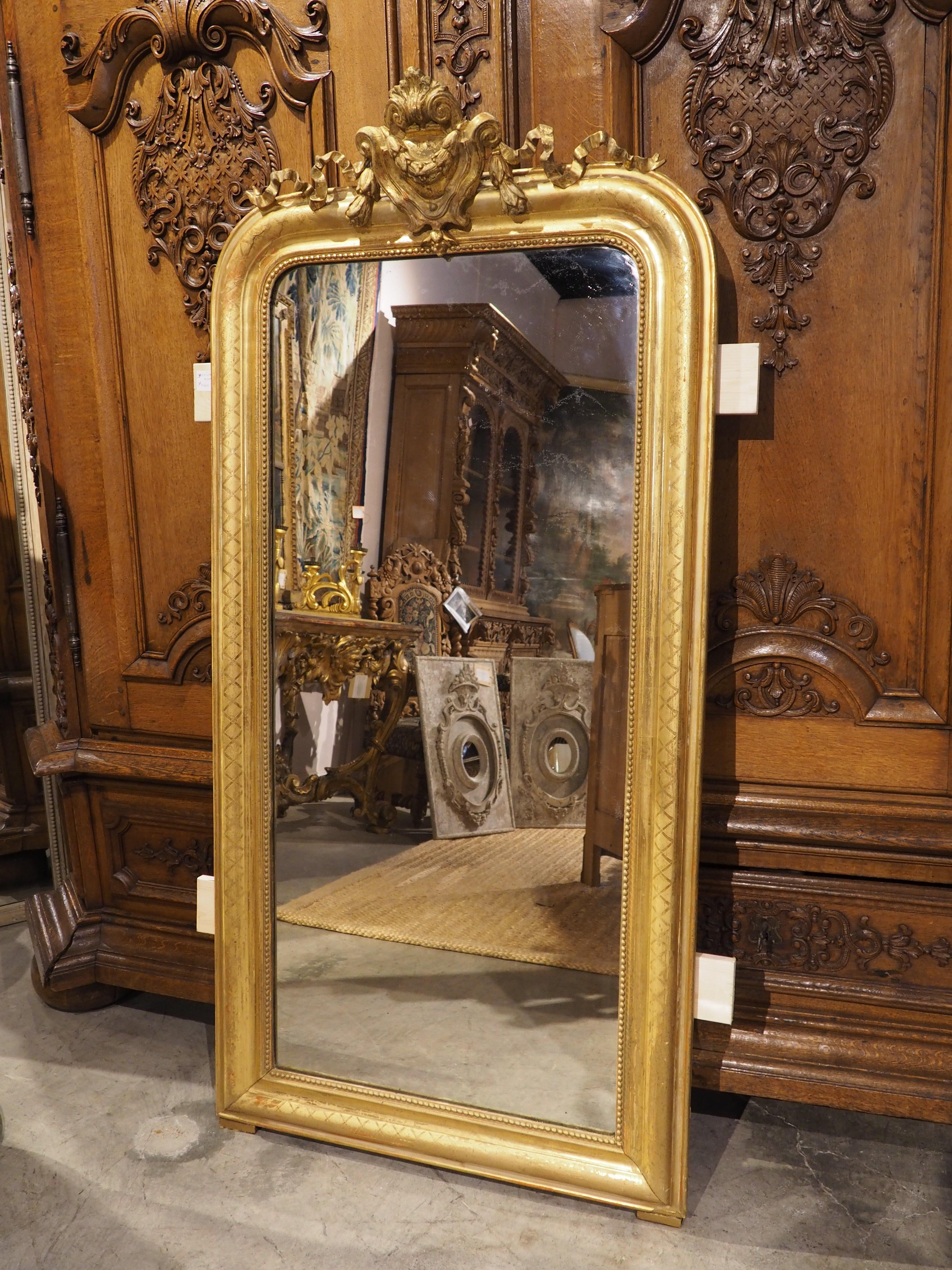 An elaborate adaptation of a timeless classic, this gold Louis Philippe mirror has a ribboned cartouche. The overall form of this French mirror from the 1800s adheres to the Louis Philippe style, with rounded upper corners and a ring of beading