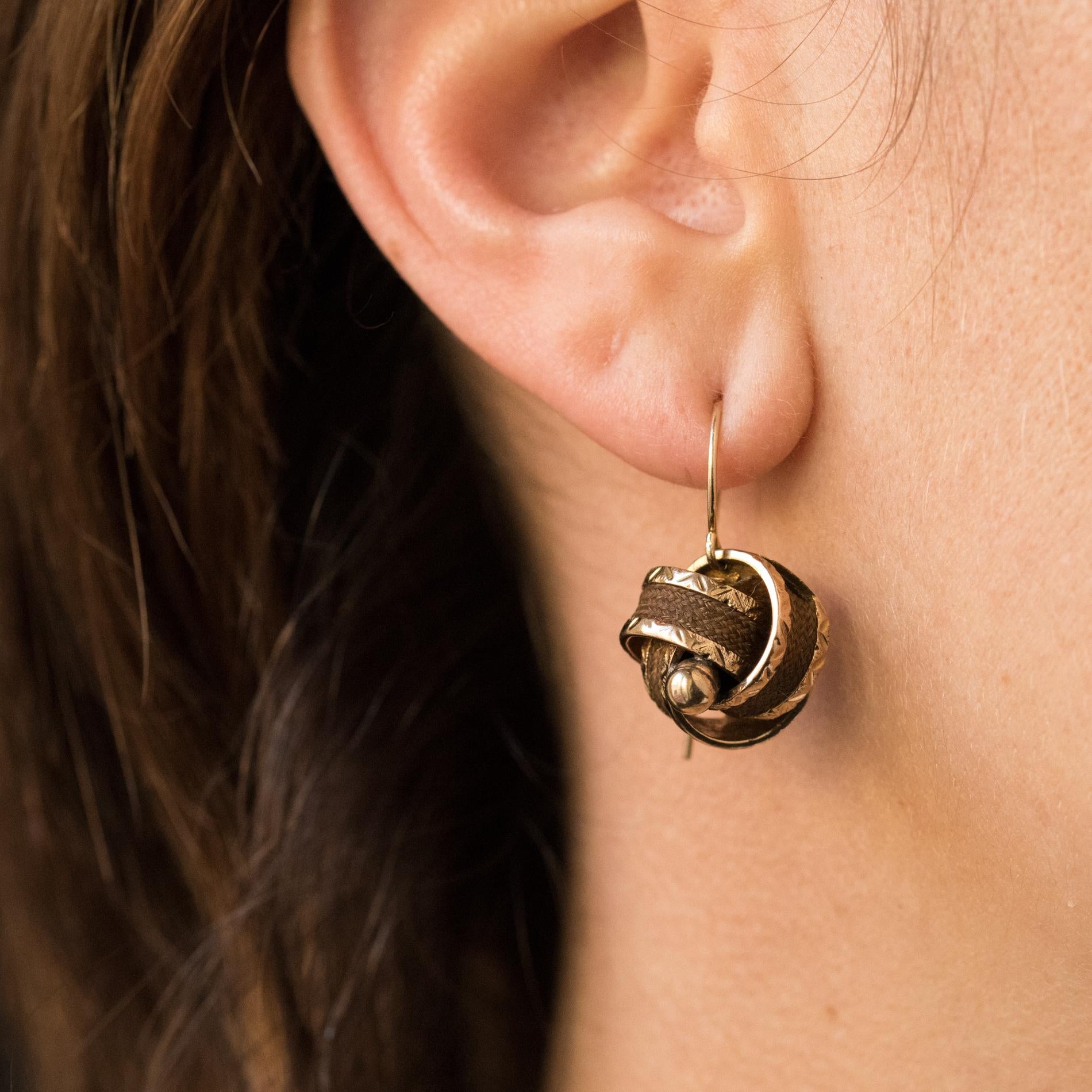 Ohrringe aus 14 Karat Gelbgold.
Jeder Ohrring besteht aus einer goldenen Schleife, in die ein Docht aus geflochtenem braunem Haar eingeflochten ist, und ist mit einer goldenen Perle besetzt. Das Befestigungssystem ist ein Schwanenhals.
Höhe: 2,4 cm,