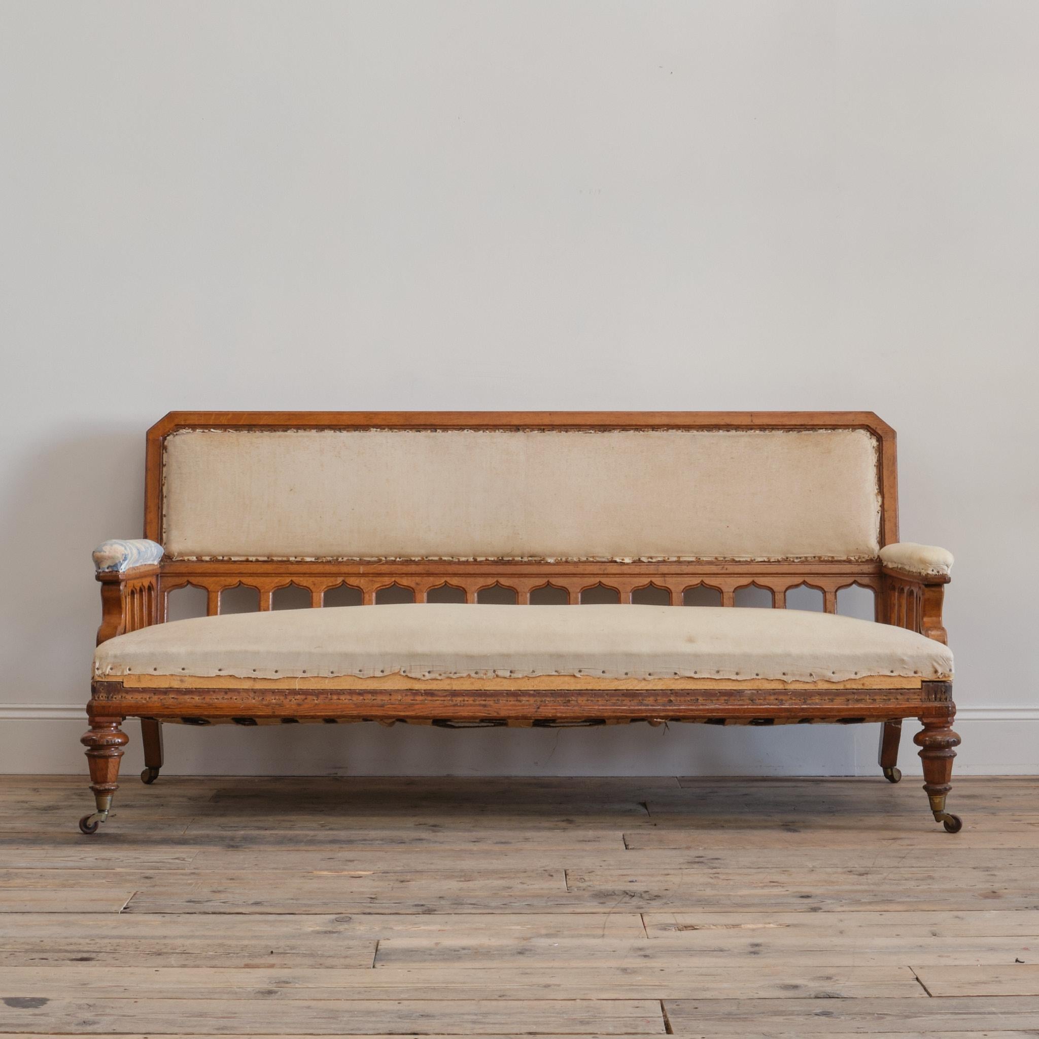 A well drawn Gothic revival 19th century country house sofa is a nice Honey coloured oak. Raised on turned and chamfered oak front legs with splayed rear legs all with the original casters. Carved arm front with pierced Gothic chamfered supports.
