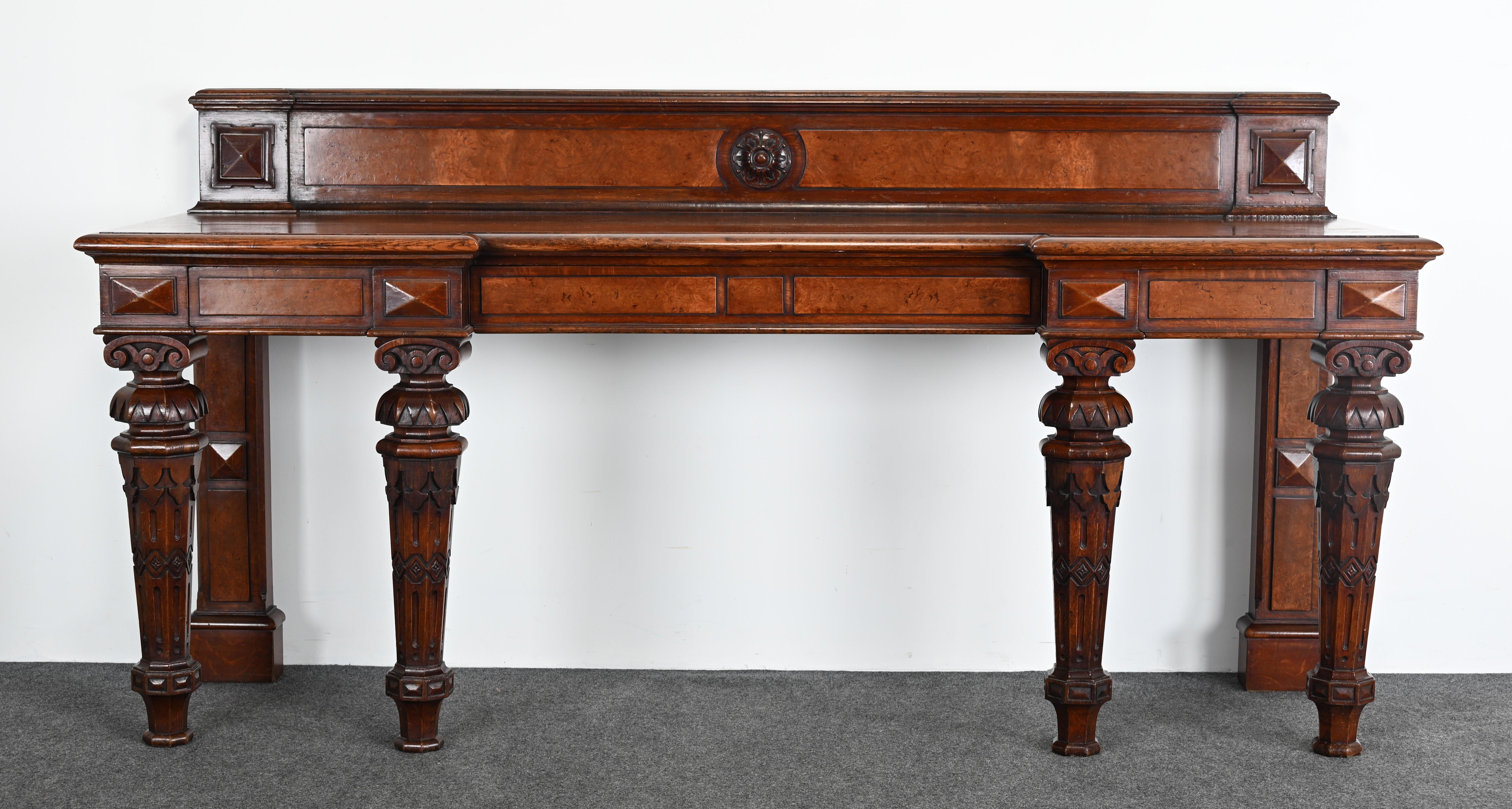 A 19th-century American Gothic-style sideboard or console table, crafted from rich, dark wood, likely chestnut. The intricate carvings on the legs, featuring ornate, architectural motifs, reflect the Gothic Revival influence popular during the