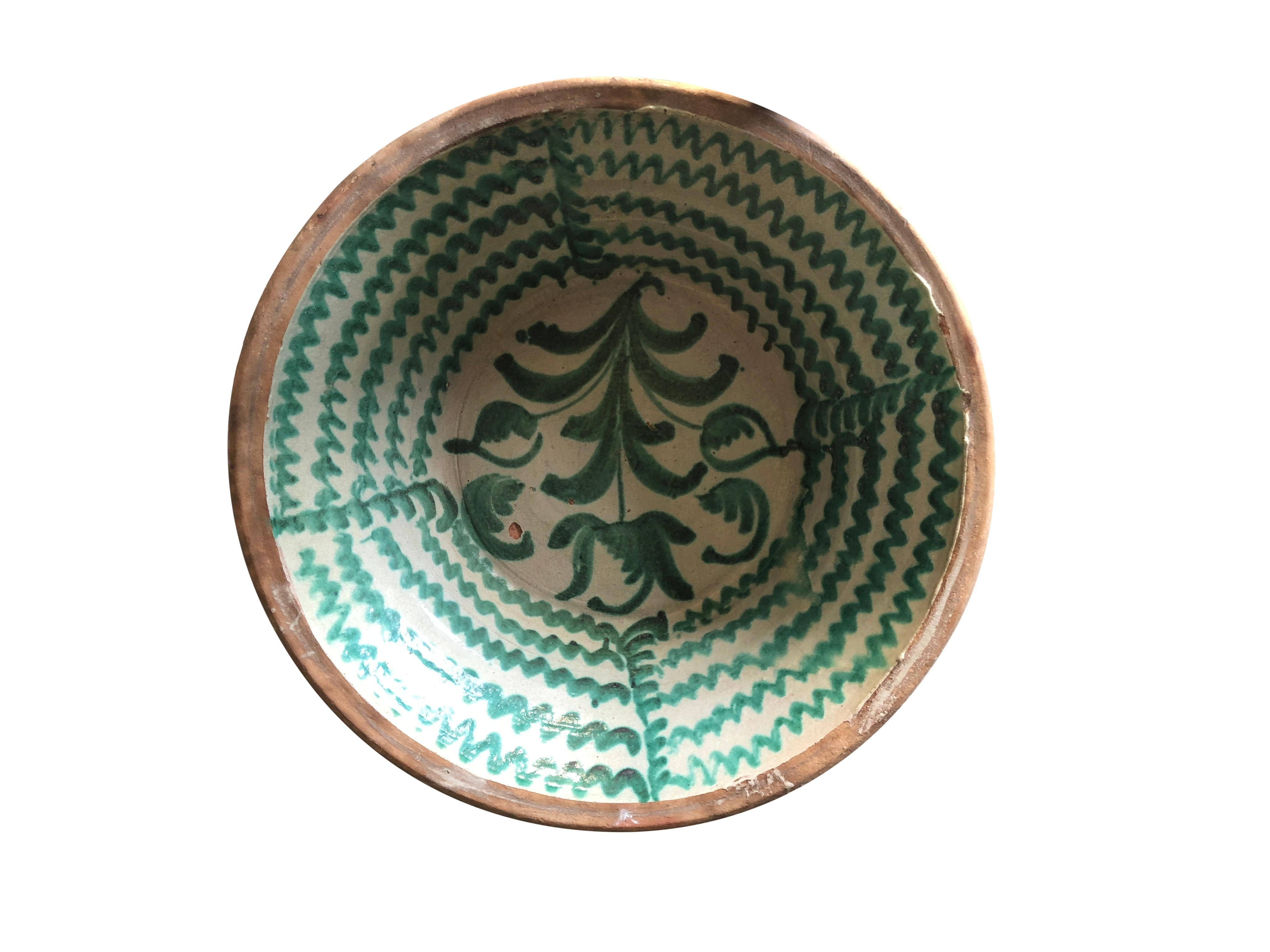 A large antique Spanish Lebrillo bowl in earthenware, made of handcrafted terracotta, in good condition. Featuring a glaze decoration in the typical Morisco green over a milk-white glaze. A large flower motif is painted to the base of the bowl