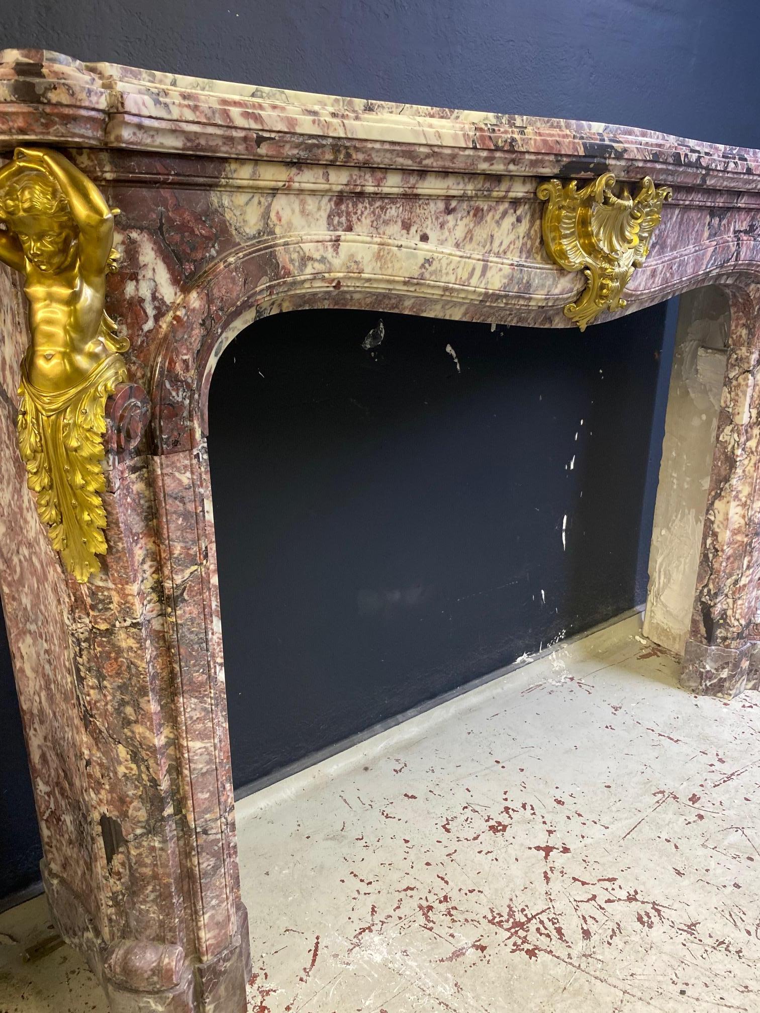 A Grand French Chateau Chimneypiece in Fleur de Peche Marble.

In the Louis XIV style, it has a serpentine shelf with moulded edge, above a sinuous frieze centred by a gilt-bronze foliage shell, the jambs each with a scrolled volute moulding headed