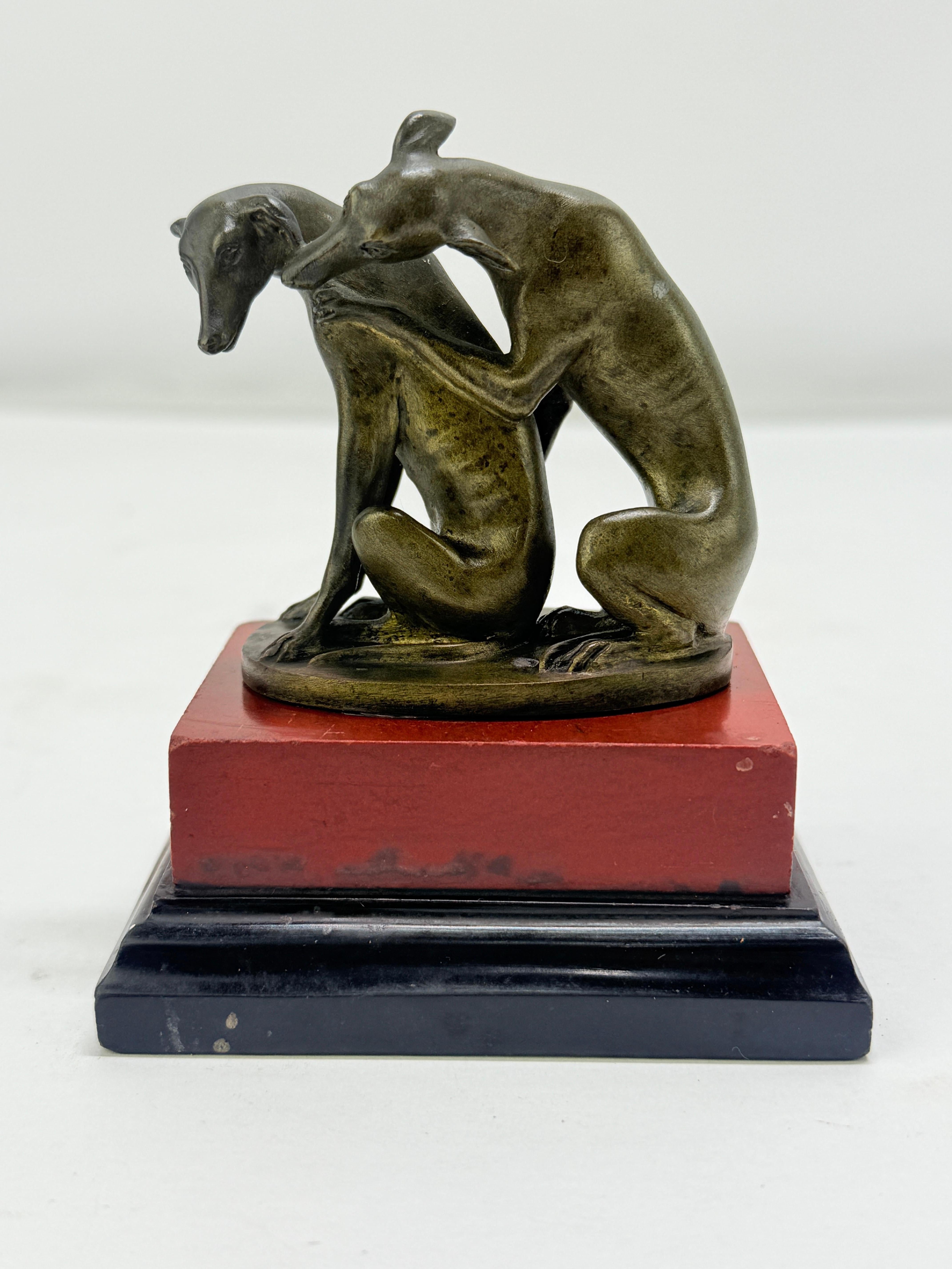 A refined Grand Tour bronze group depicting two affectionate whippets, French, late 19th century, modeled with elegant naturalism and subtle emotional depth. One hound sits with quiet poise, while the other leans tenderly against its companion, paw