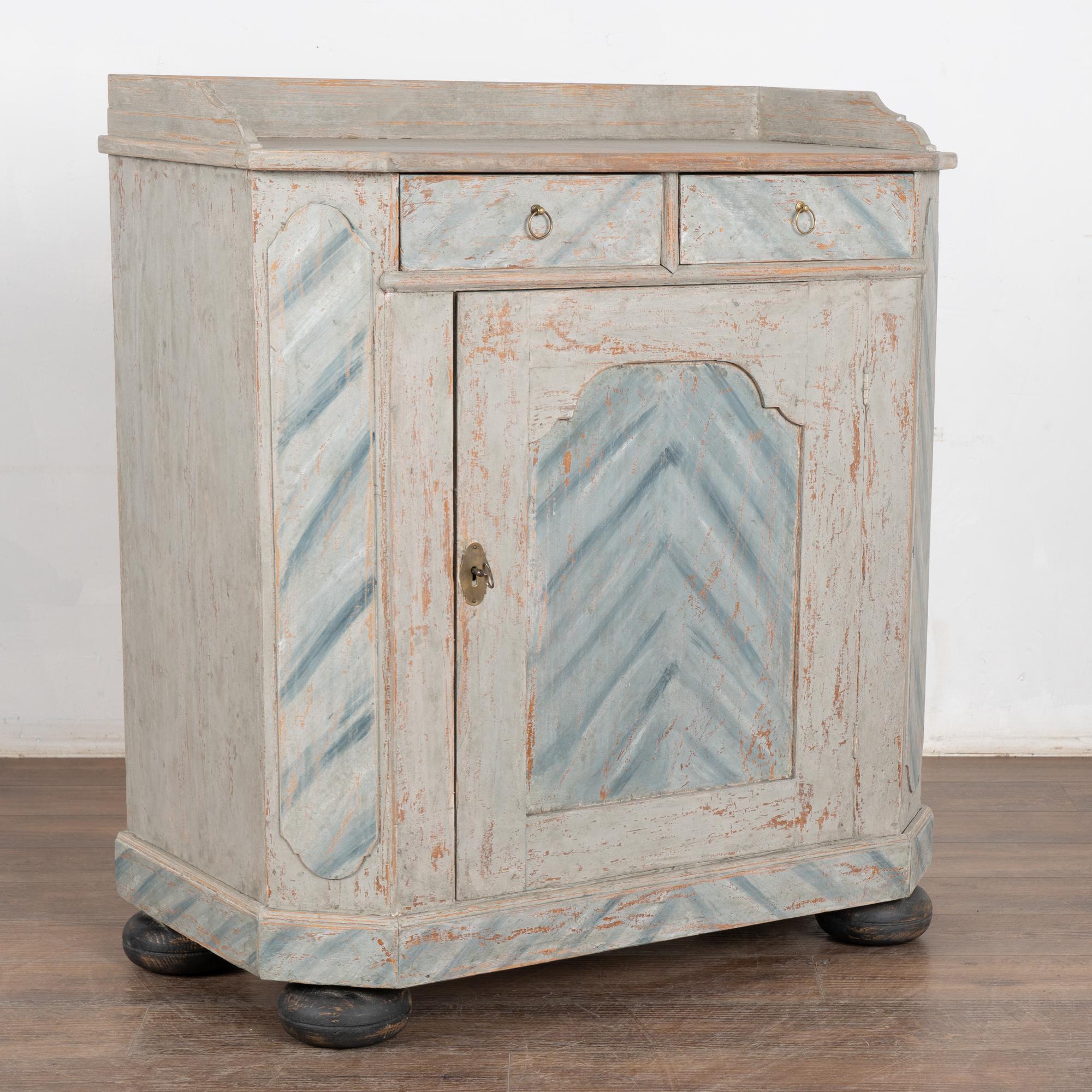 The soft gray finish has been gently distressed, bringing out the warm patina of the pine below in this lovely sideboard from Sweden. 
The folk art style of the contrasting white and blue motif highlight the panels, drawers and skirt.
Restored,