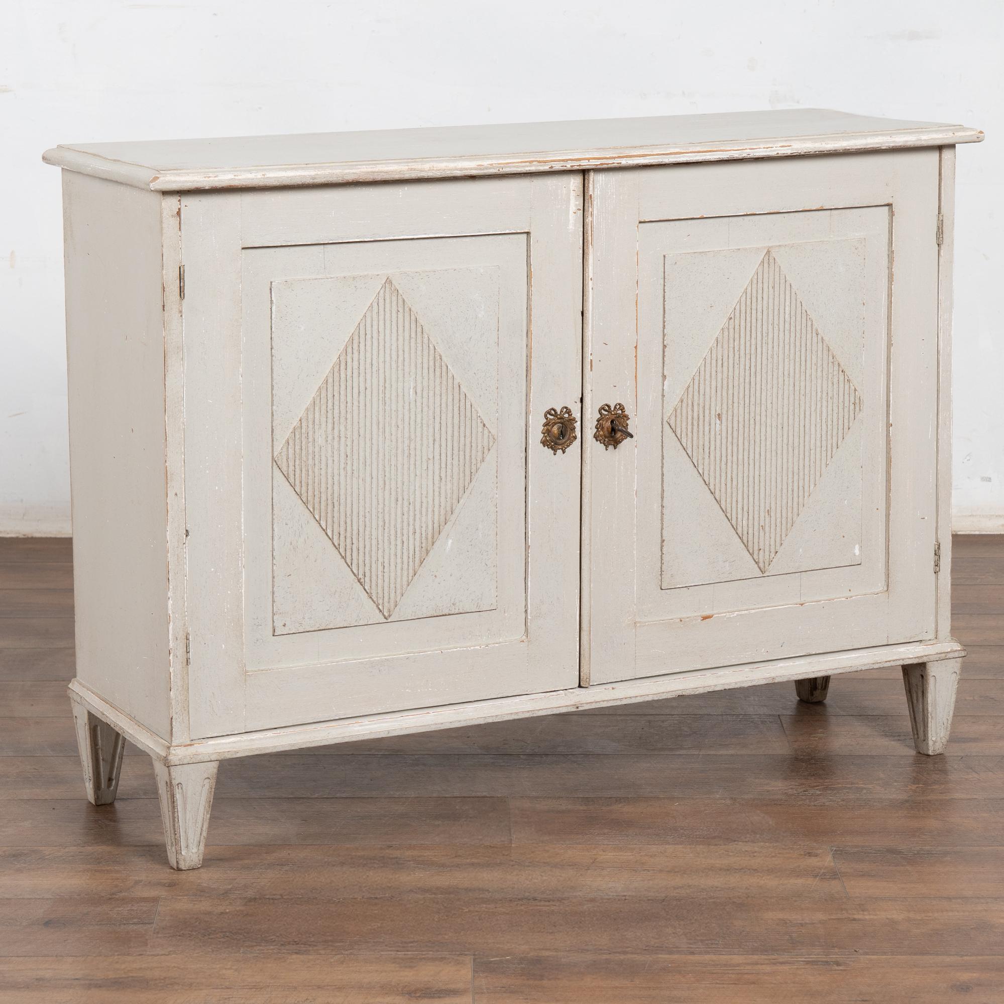 Credenza svedese in pino gustaviano del XIX secolo con una nuova finitura a strati dipinta in grigio chiaro con sfumature bianche. La finitura è leggermente sbiadita, rivelando il pino naturale sottostante e adattandosi all'età di questo piccolo