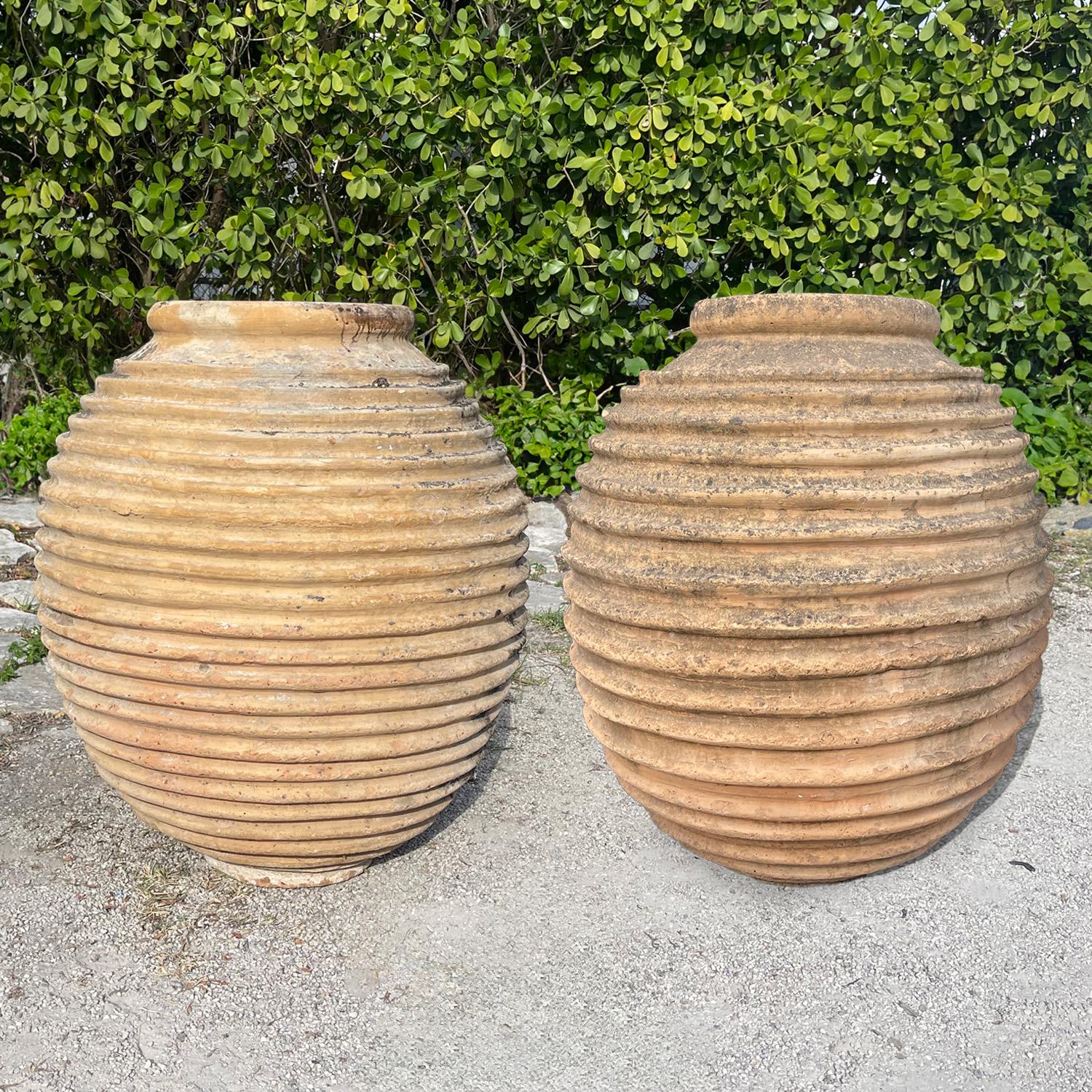 A pair of large antique Greek Koroniotiko olive oil jars, each featuring the traditional hand crafted ribbed Nekuma decoration across their rounded terracotta forms, in good condition. Originally used for storage and transport, these vessels ors