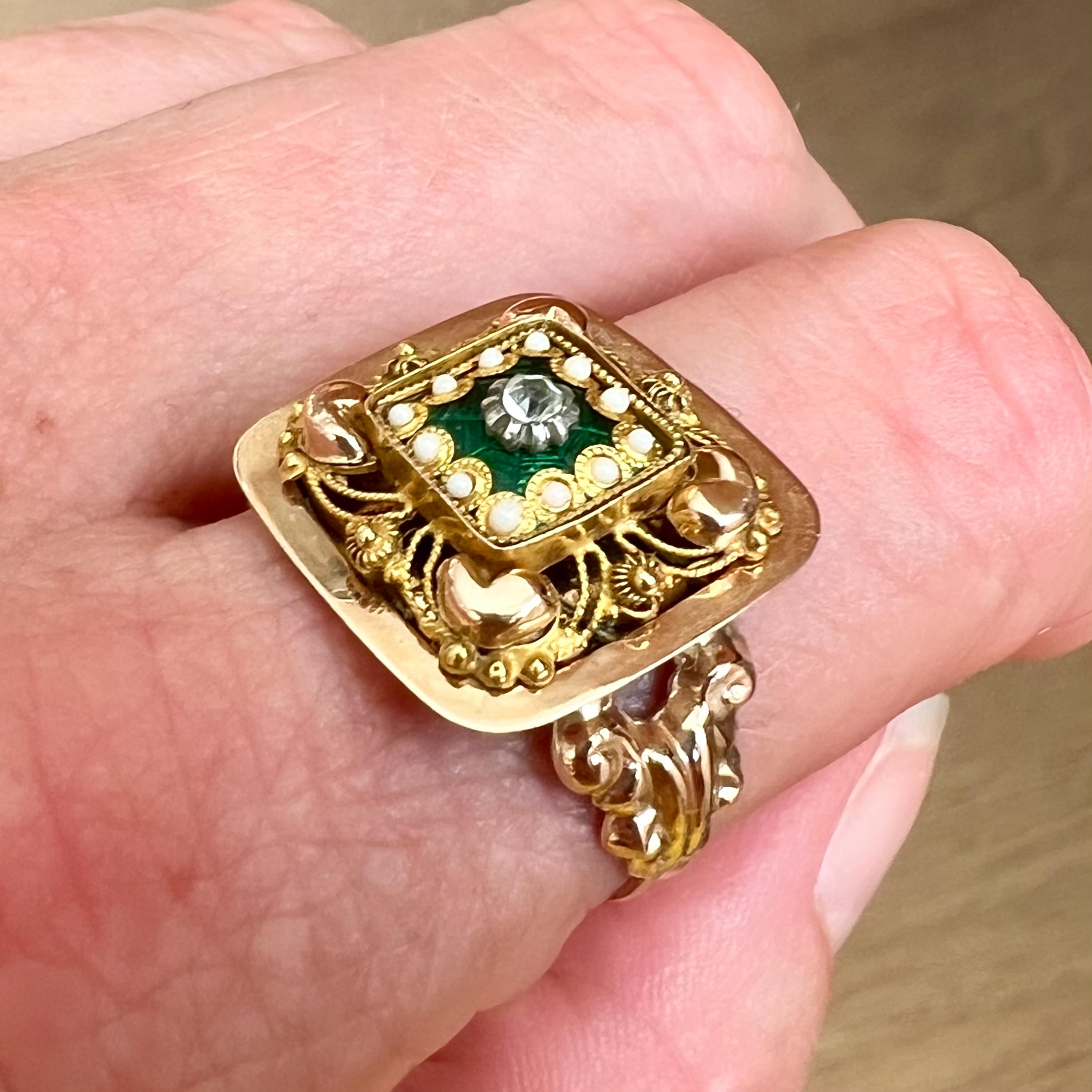 This is an antique square shaped 14 karat yellow gold ring set with green enamel, seed pearls and a  rhinestone. The design of this Victorian ring is made with beautiful filigree and cannetille work around a smaller square with twelve seed pearls