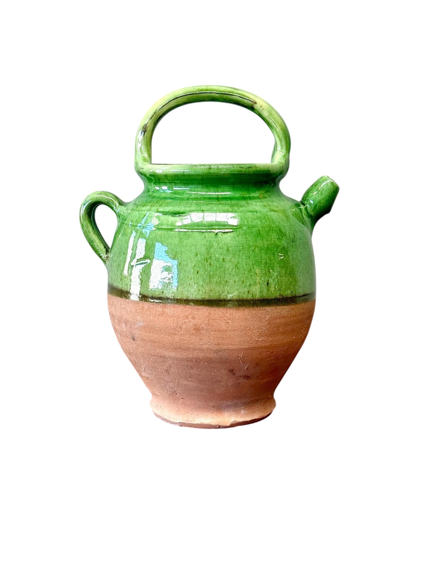 Ce charmant pot à eau français du XIXe siècle est un bel exemple de poterie provençale traditionnelle, qui se distingue par sa glaçure vert vif et sa silhouette régionale distinctive. Façonné à la main en terre cuite et partiellement trempé dans une