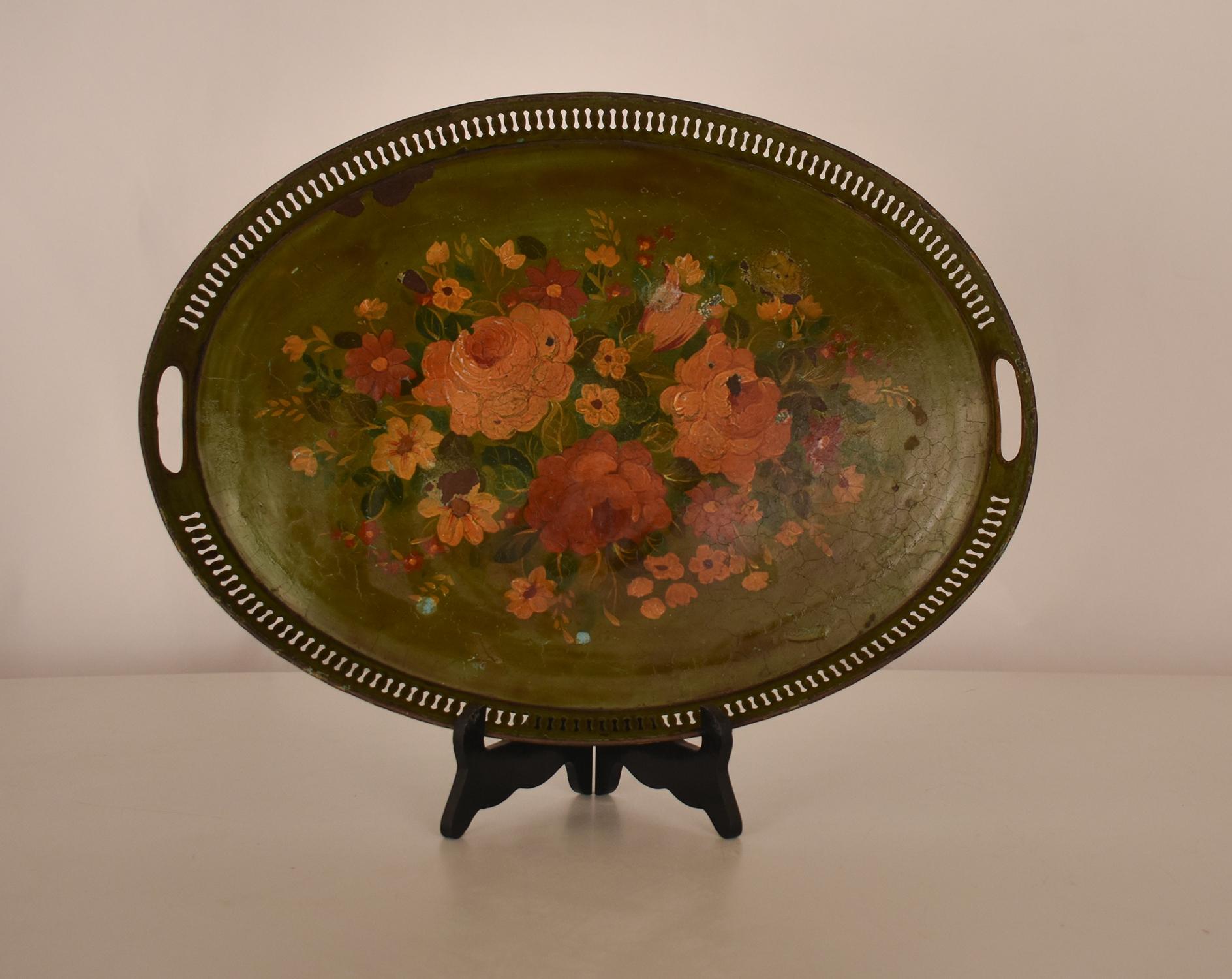 An antique French oval-shaped tray, made of metal and painted with flowers on its surface, with a green background. This particular tray is of French origin and dates back to 1960.