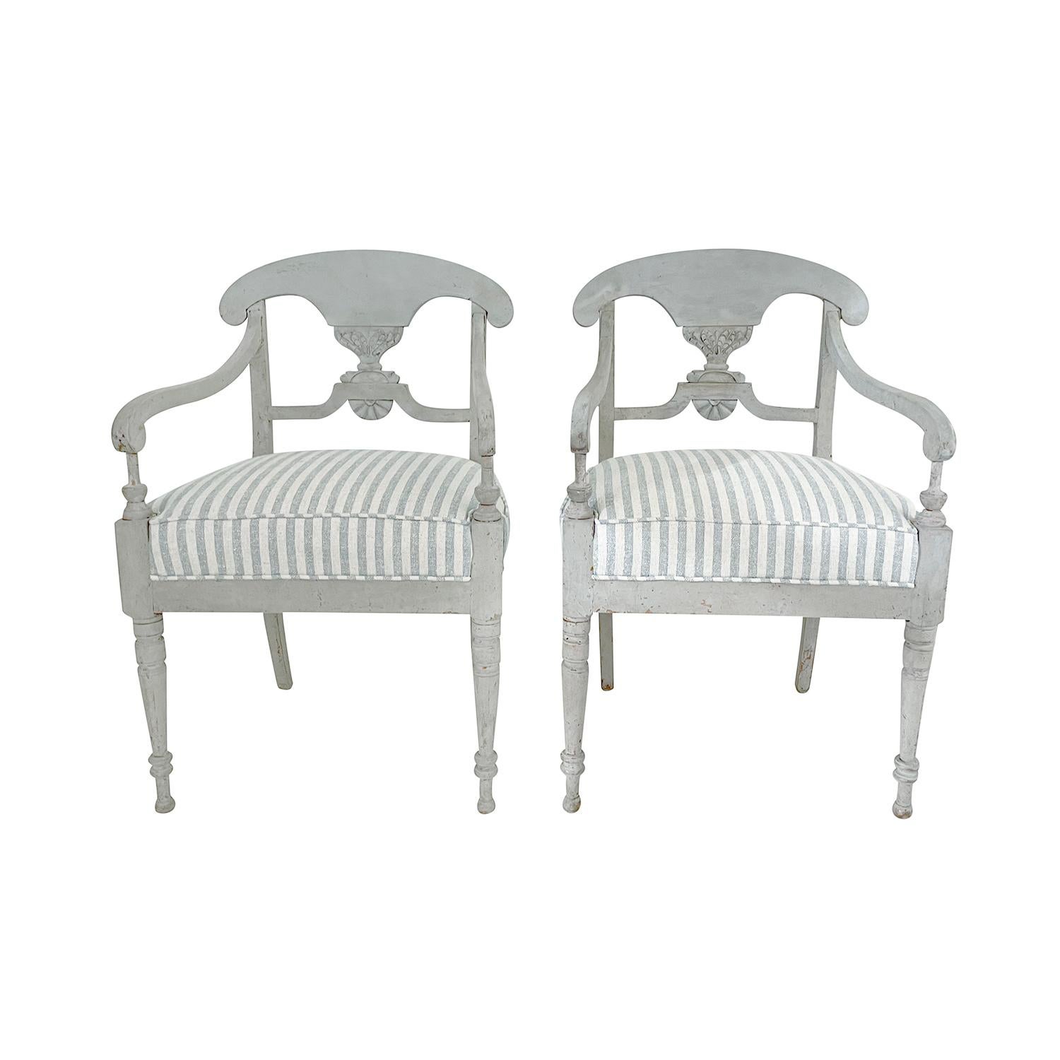A light-grey, antique Swedish Gustavian pair of armchairs made of hand crafted painted Pinewood, in good condition. The Scandinavian side chairs have an open, arched backrest, standing on four particularized legs, detailed in the Neoclassical Greek