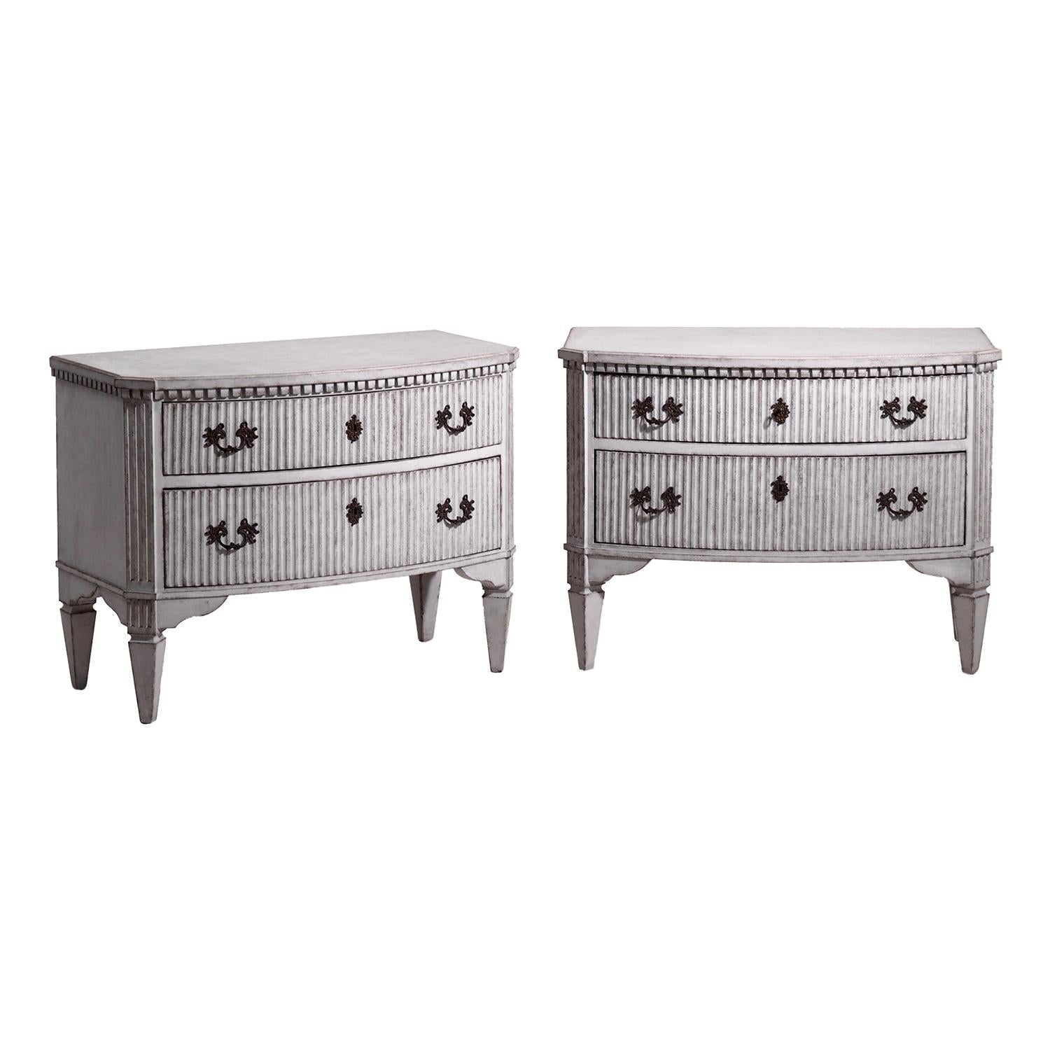An antique Swedish Gustavian pair of grey chests made of hand carved Pinewood with two drawers, standing on four fluted carvings and tapered legs, in good condition. The commodes are detailed in the Neoclassical Greek style with their original
