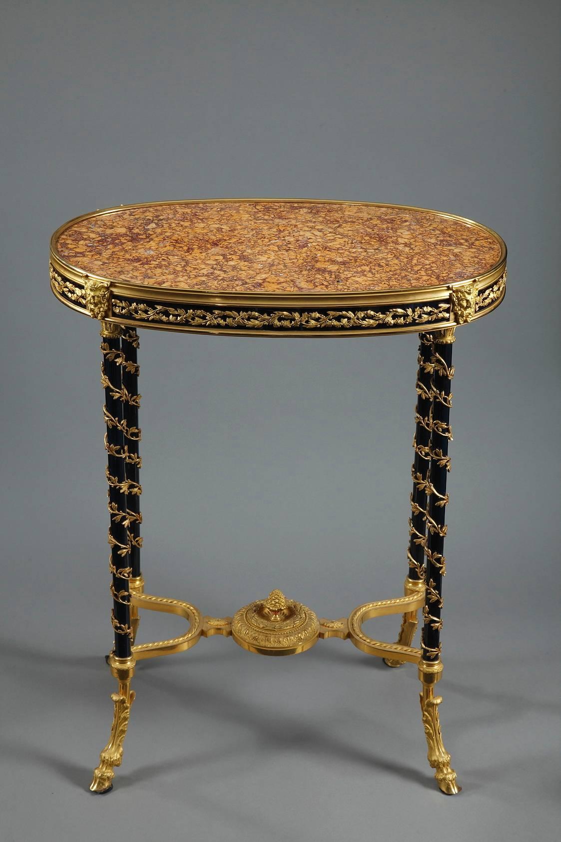 Oval gueridon featuring a marble top. The purple brocatelle marble originates from Spain and is ringed by a gilt bronze rim decorated with intertwined foliage on a dark blue background. Satyr heads are placed at the top of each of the slender table