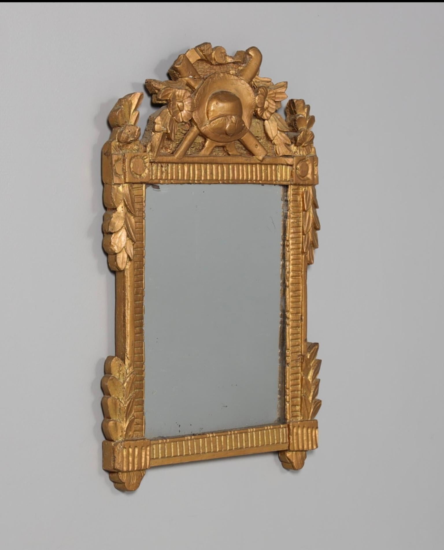 Specchio di epoca gustaviana, in legno intagliato e dorato, con decorazione a foglie d'acanto sui lati e un trofeo sulla parte superiore.