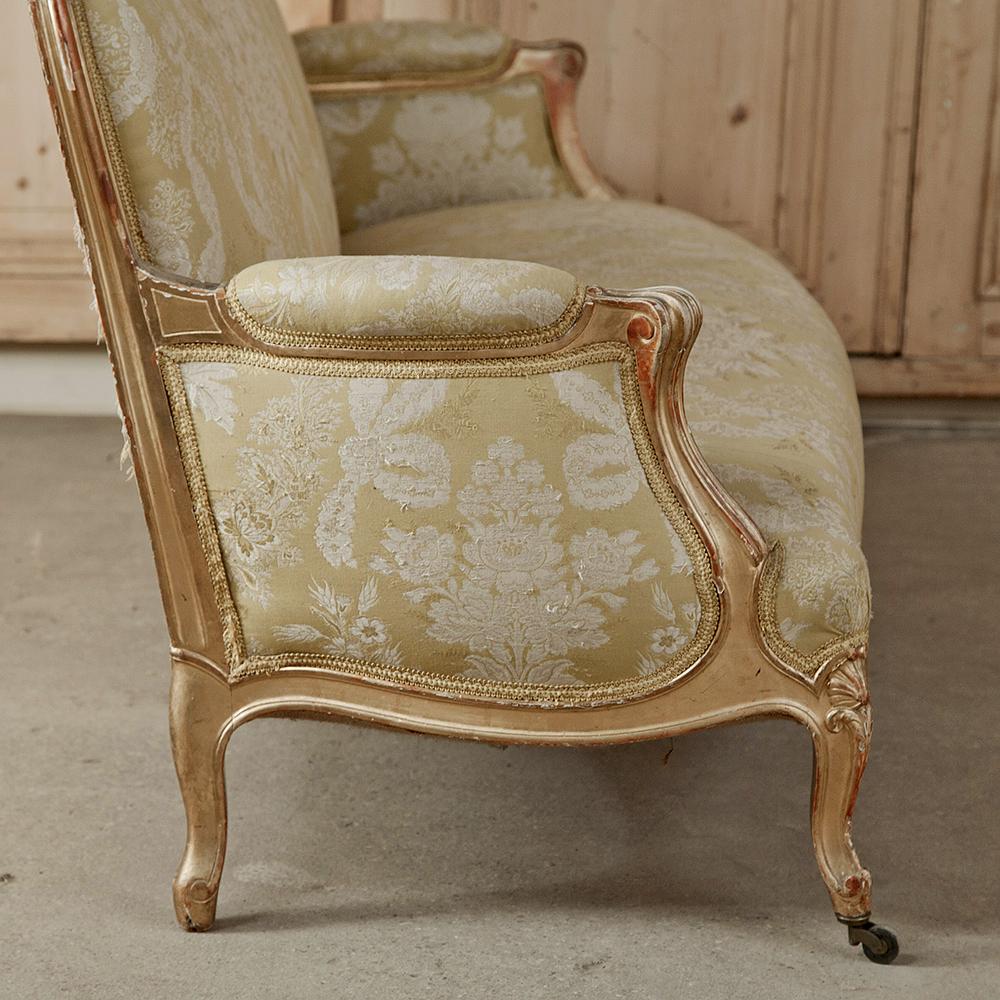 19th century hand carved antique Italian gilt-wood Rococo sofa is an absolutely fantastic large-scale piece lavished with damask fabric on sculpted Louis XV-inspired frame with gilded finish. The opulent Italian rococo design style has influenced