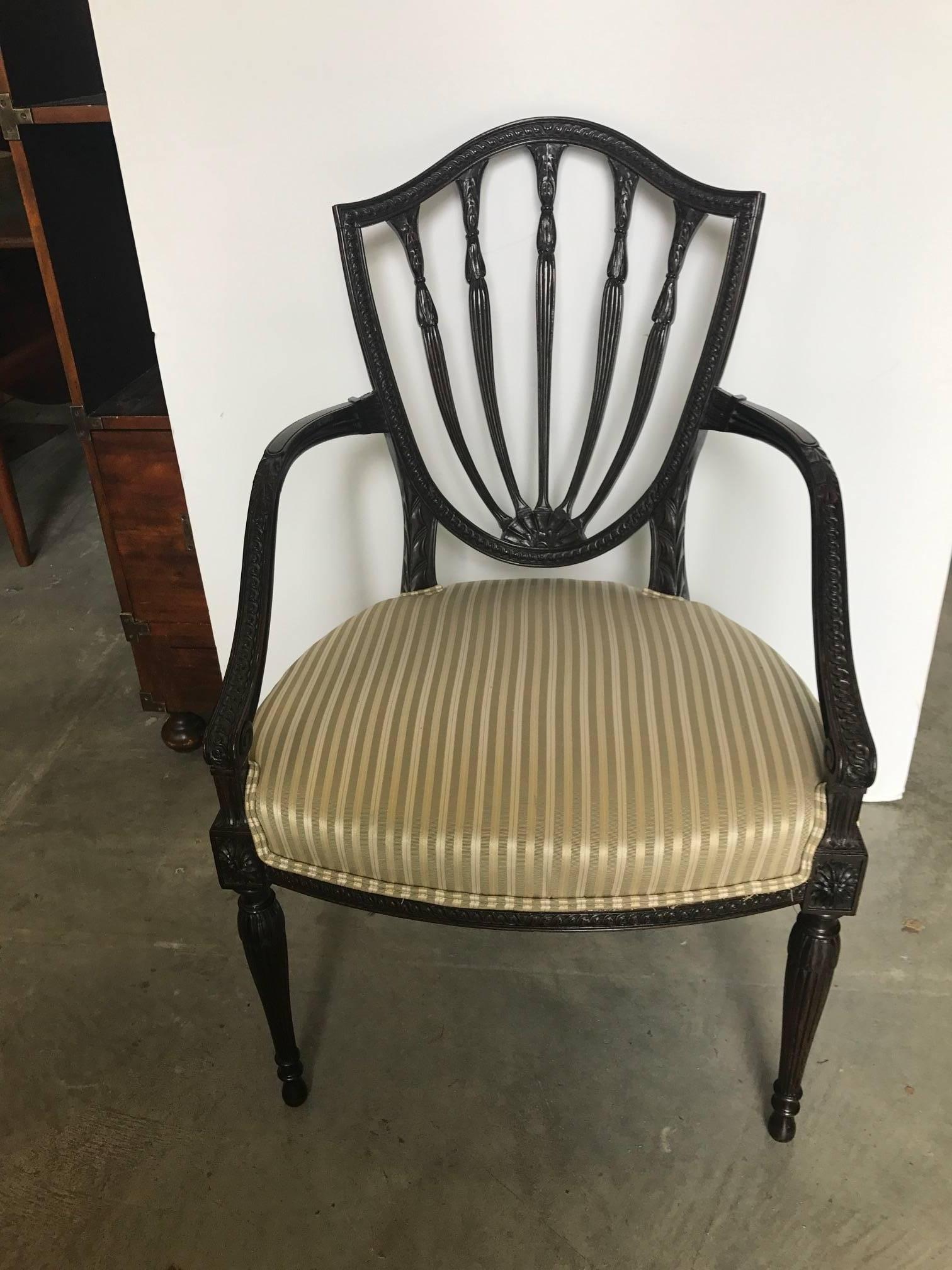 Elegant and graceful hand carved mid-19th century shield back Hepplewhite armchair. The dark mahogany frame is expertly carved all along the frame. The corners have rosettes with tapered reeded legs. The seat is an hourglass coil spring construction