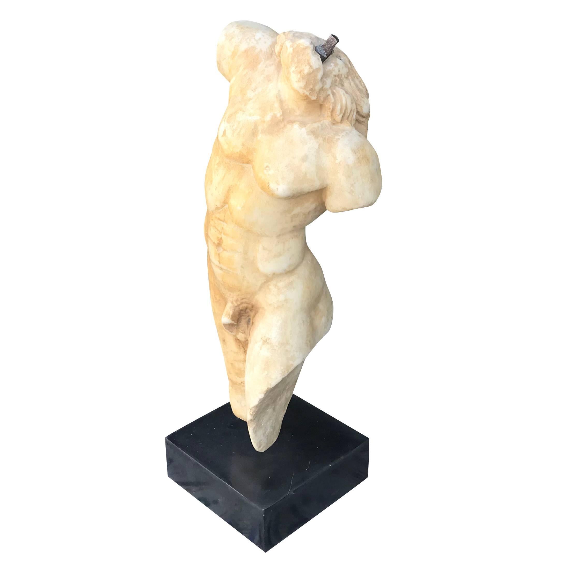 A hand-carved marble torso in Carrara marble mounted onto a square black marble base from Italy, circa 1880. Though the fragment lacks the head, arms and legs, the well formed body maintains the strength of movement.