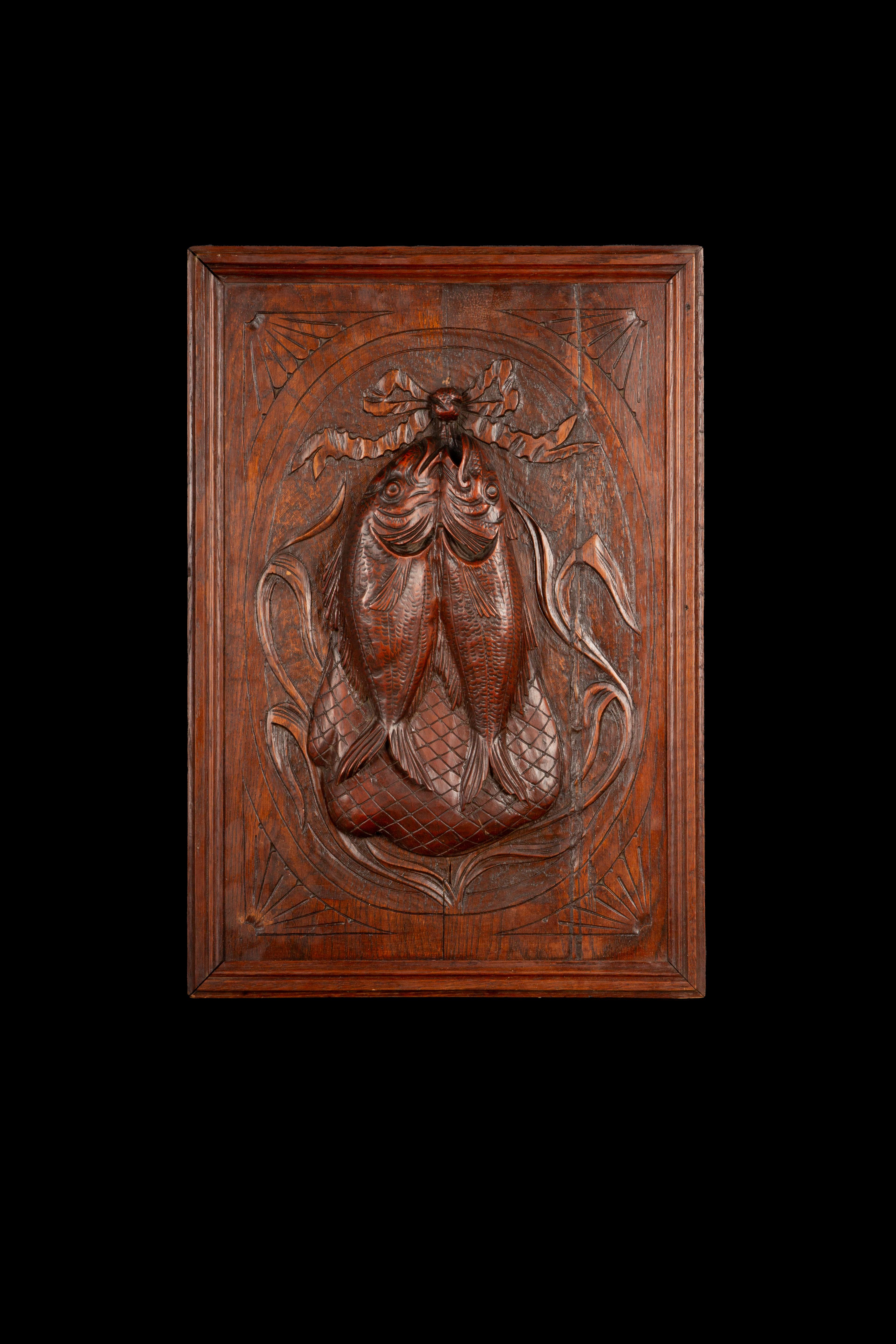 A finely hand-carved oak panel, skillfully depicting two intricately detailed fish hanging in front of a creel basket. This beautifully rendered relief captures the texture and lifelike quality of the fish, enhanced by the flowing lines and depth of