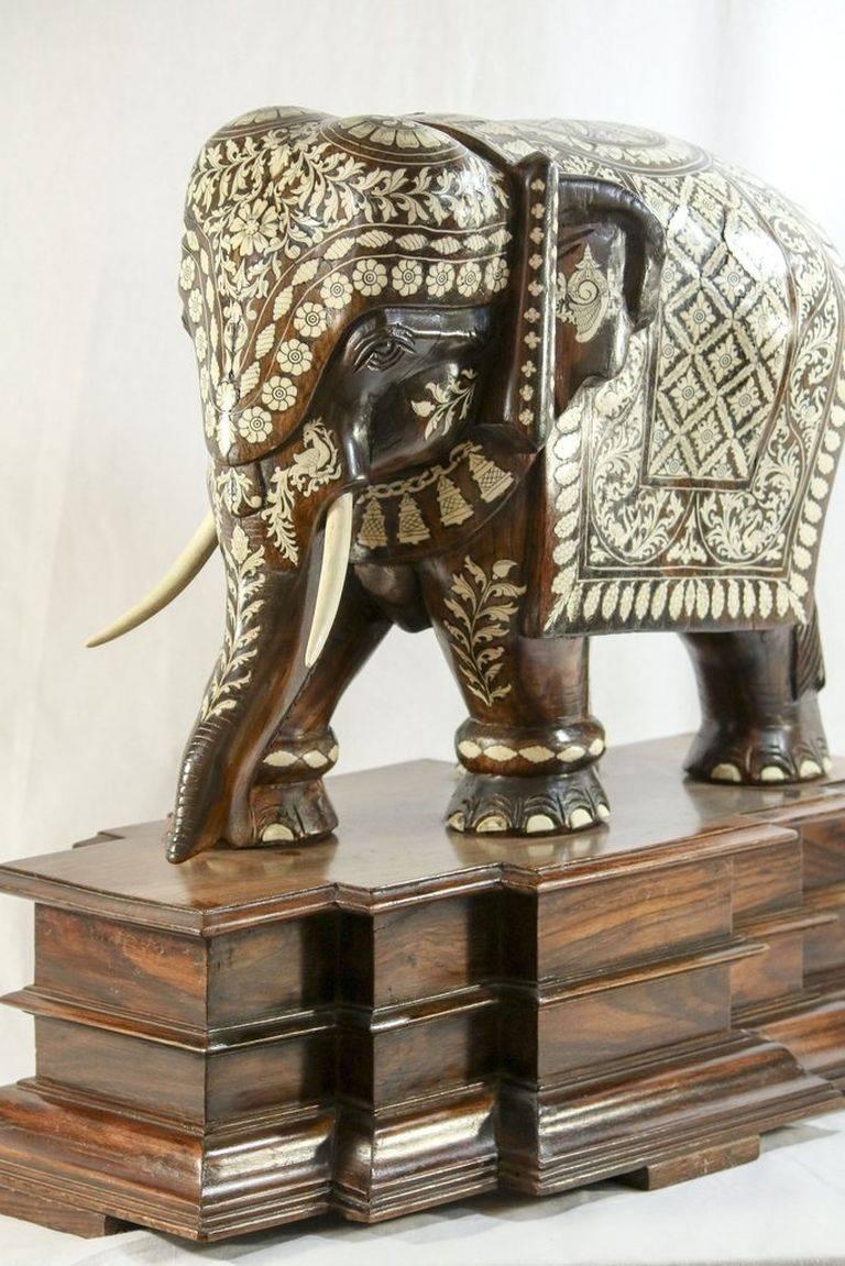 Anglo-Indian elephant figure hand-carved from a single rosewood block with exquisite camel bone inlay featuring stylized peacocks amid trailing vine leaves, other foliate and medallion flowers. The caparisoned mammoth is draped in a celebratory