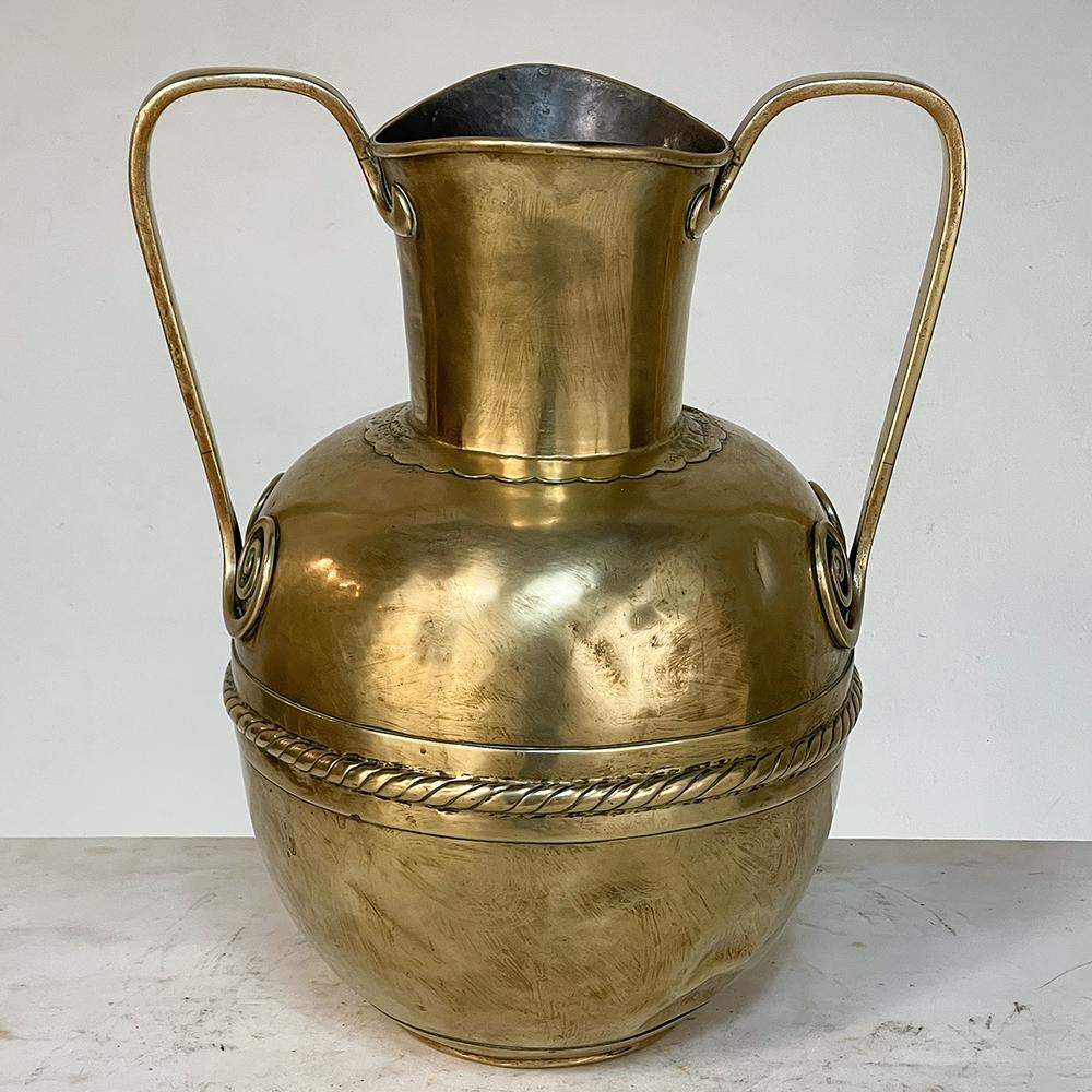 Il vaso a doppio manico in ottone martellato a mano del XIX secolo è il prodotto di un talentuoso fabbro e presenta un design interessante con abbellimenti altrettanto interessanti! L'apertura ovoidale nella parte superiore è stata progettata per