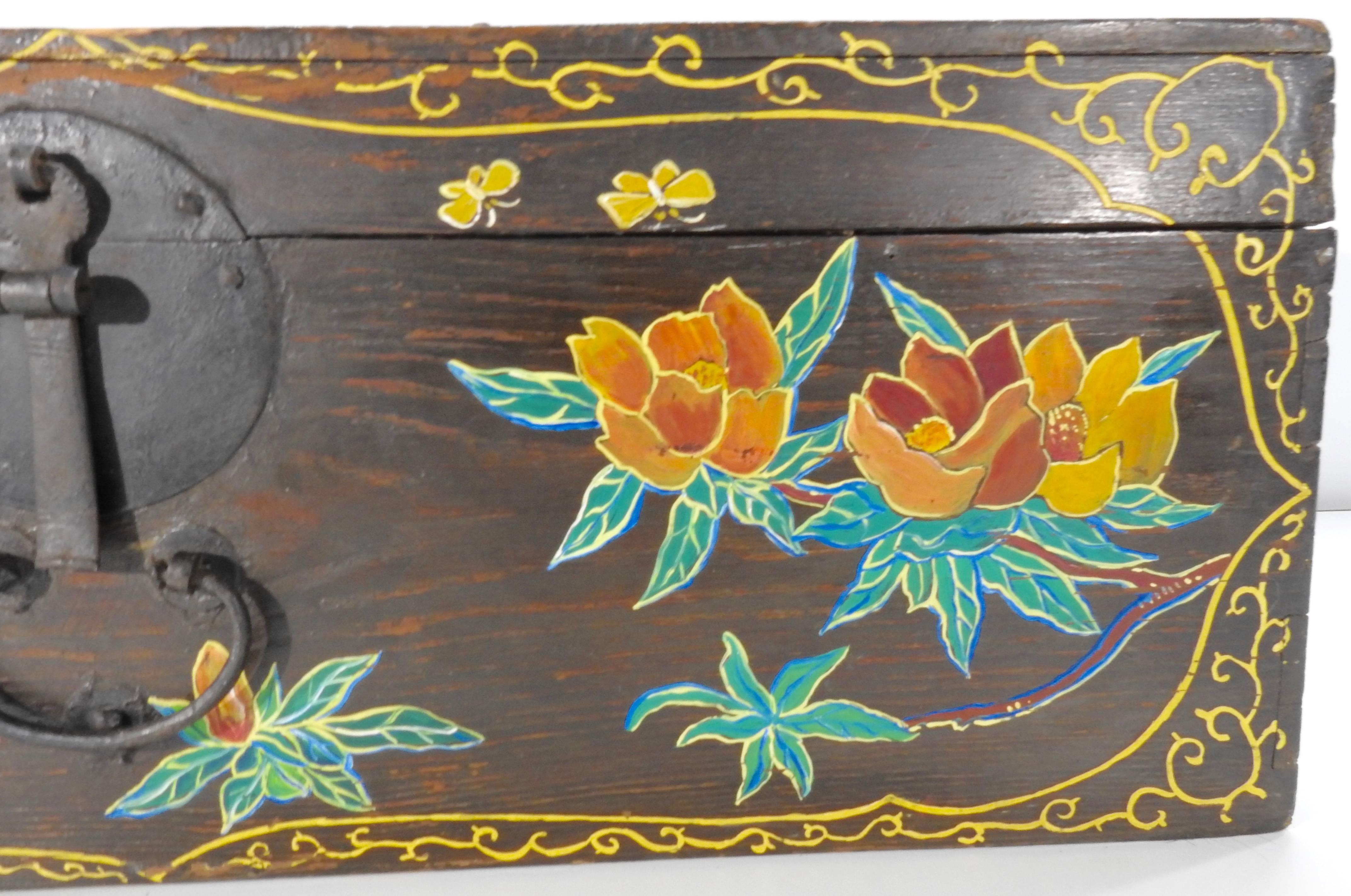 Birds and flowers embellish the front of this wooden trunk along with a scrolling border. Soft shades of yellow, orange and green make up the artwork and the painting appears to be a mid-20th century embellishment. A cast iron latch completes the