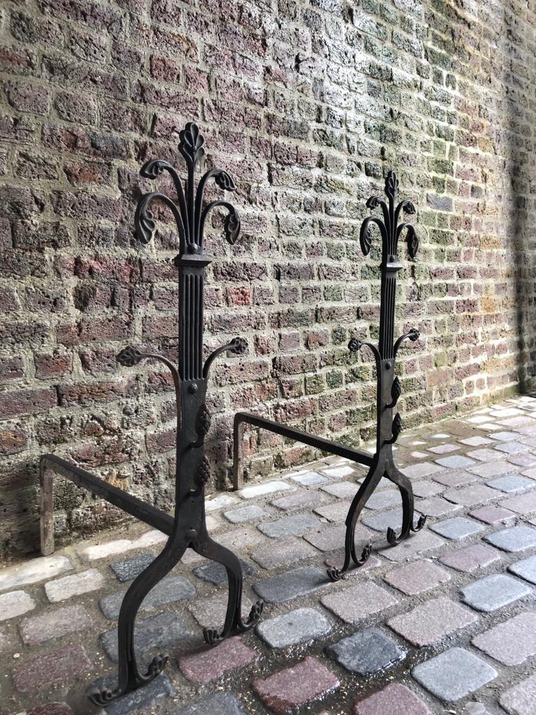A large pair of 19th century handwrought iron gothic fireplace andirons firedogs. This pair are completely wrought by hand out of very thick iron and have a dark black finish, crafted with swirled legs and shafts with beautifully wrought floral
