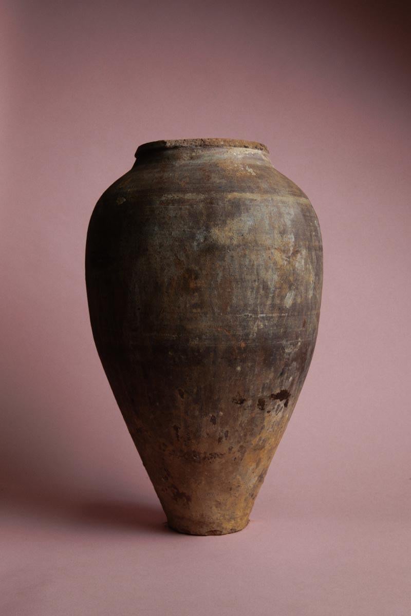 Questo vaso turco conico del XX secolo è un esempio di ceramica mediterranea fatta a mano, originariamente utilizzata per conservare alimenti o cereali. Il suo design affusolato gli conferisce un profilo elegante e allungato, rendendolo funzionale e