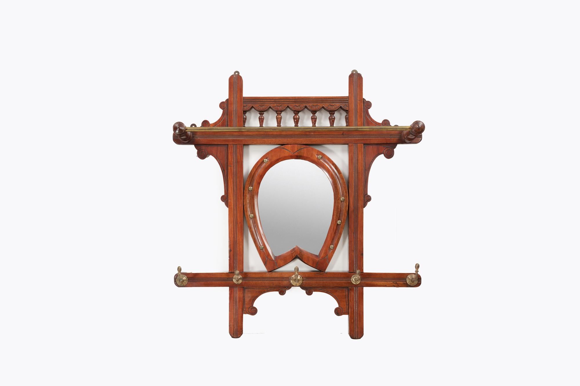 19th Century hanging hall rack with decorative central horseshoe shaped mirror with bevelled plate and brass studs. This piece is complete with turned supports, carved panels, brass hanging hat hooks and a brass hanging rail. Circa 1880.