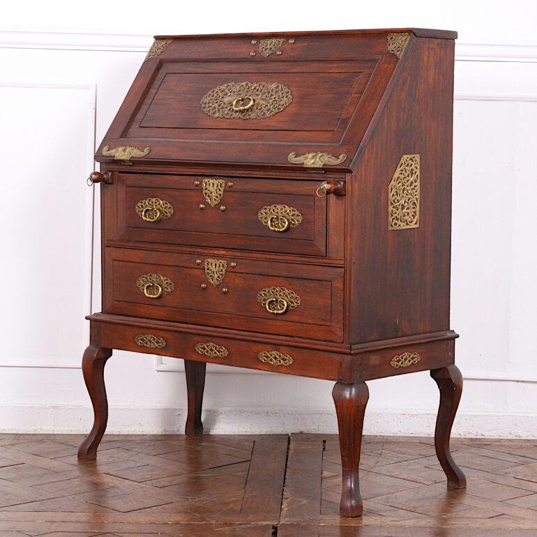 A hardwood slant-front desk or bureau on carved stand, embellished with ornate pierced brass fittings and hardware and with a fitted interior with several slots and a small cupboard. Two larger drawers below the writing surface and a pair of