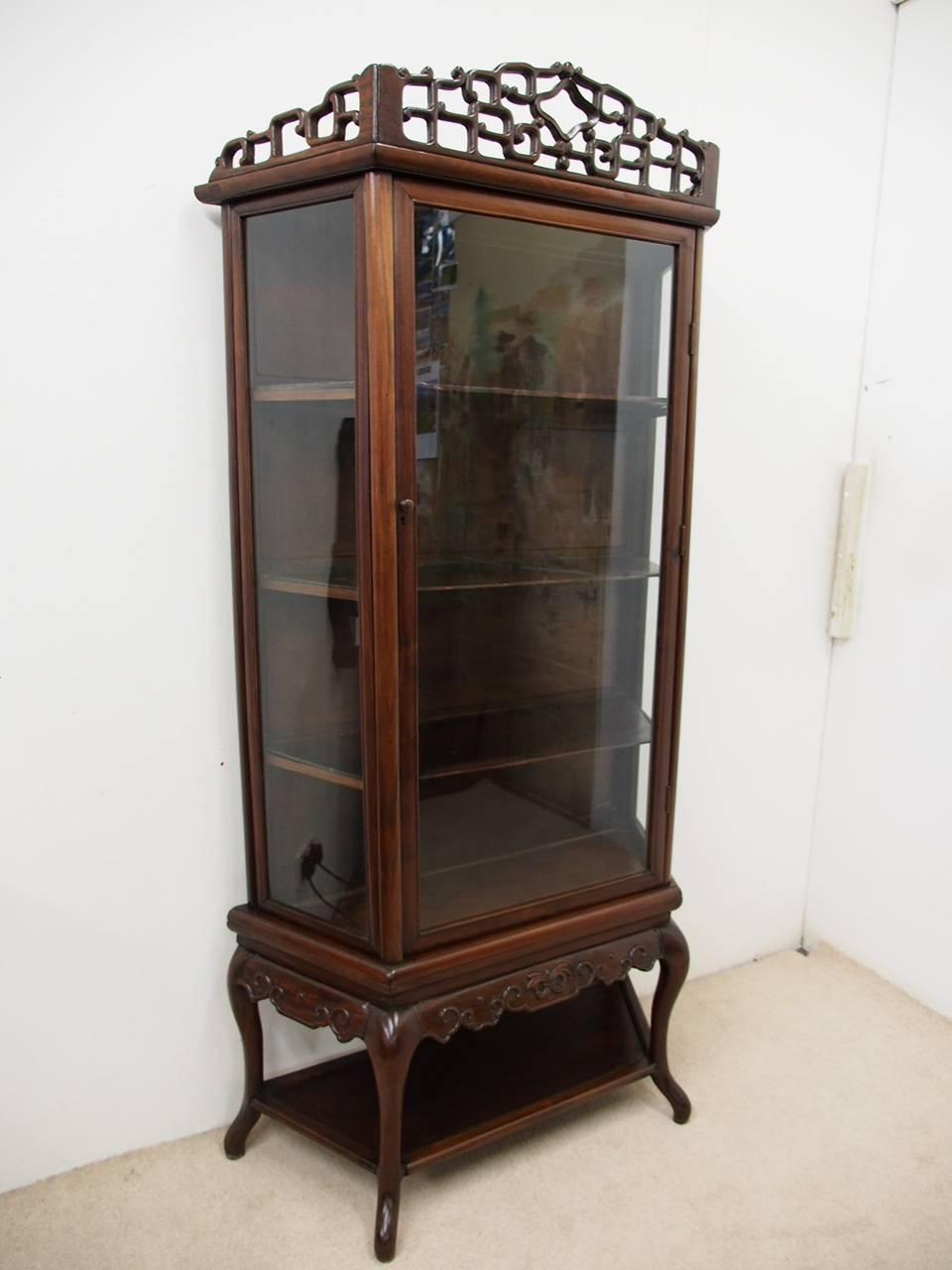 Hardwood display cabinet, circa 19th century. The top has a key pattern carved gallery above a central glazed door, flanked by glazed panel sides. With a shelved interior, it is all raised on a separate base with relief carved detailing and sits on