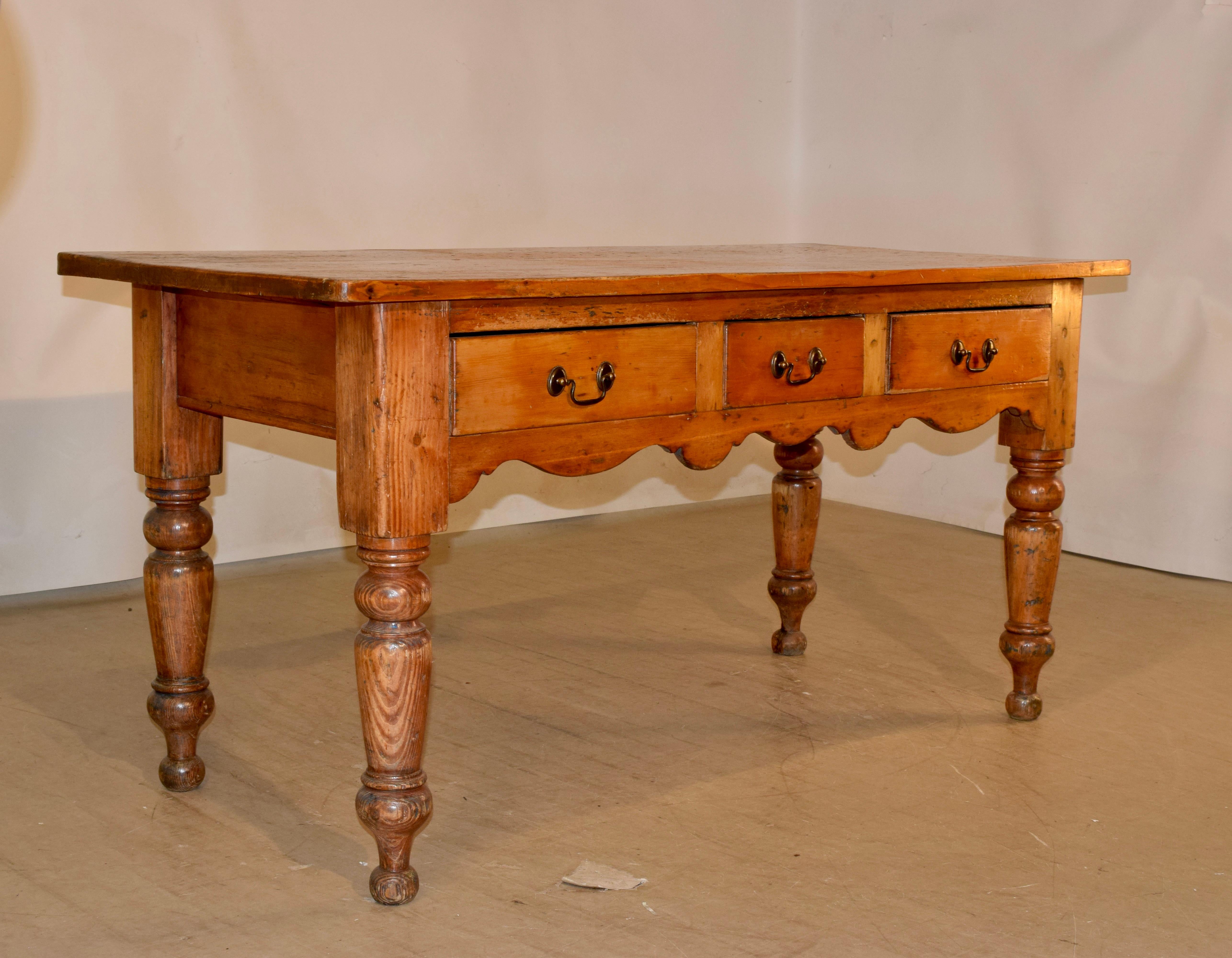 19th century pine harvest table made in the English region of Lancashire. The top is made up of planks and follows down to a scalloped apron with three drawers in the front, supported on wonderfully hand turned legs. The finish is rustic from age