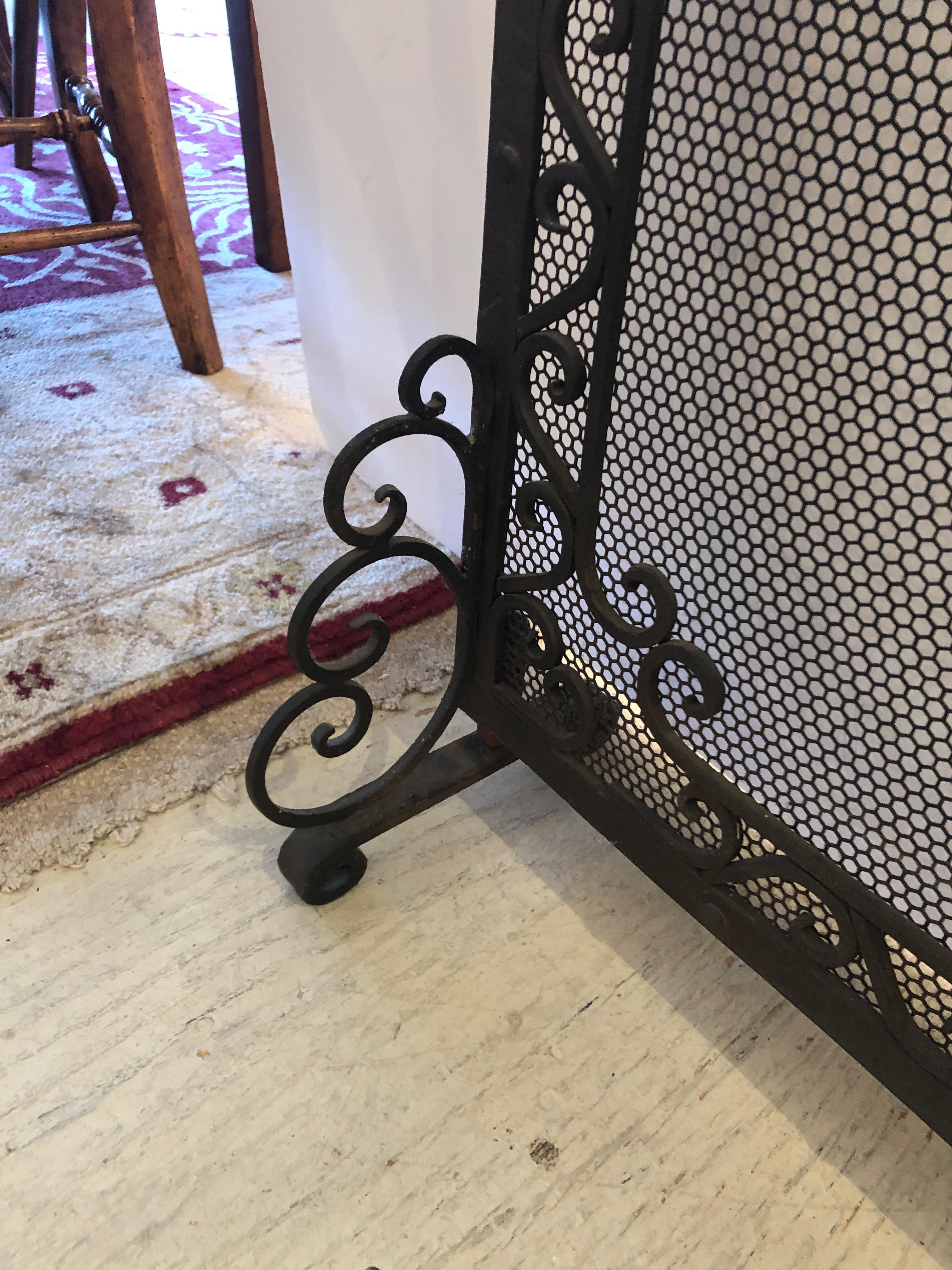 A stunning heavy and beautifully made antique freestanding fireplace screen constructed of black handwrought iron having scroll feet, handles, and honeycomb mesh.