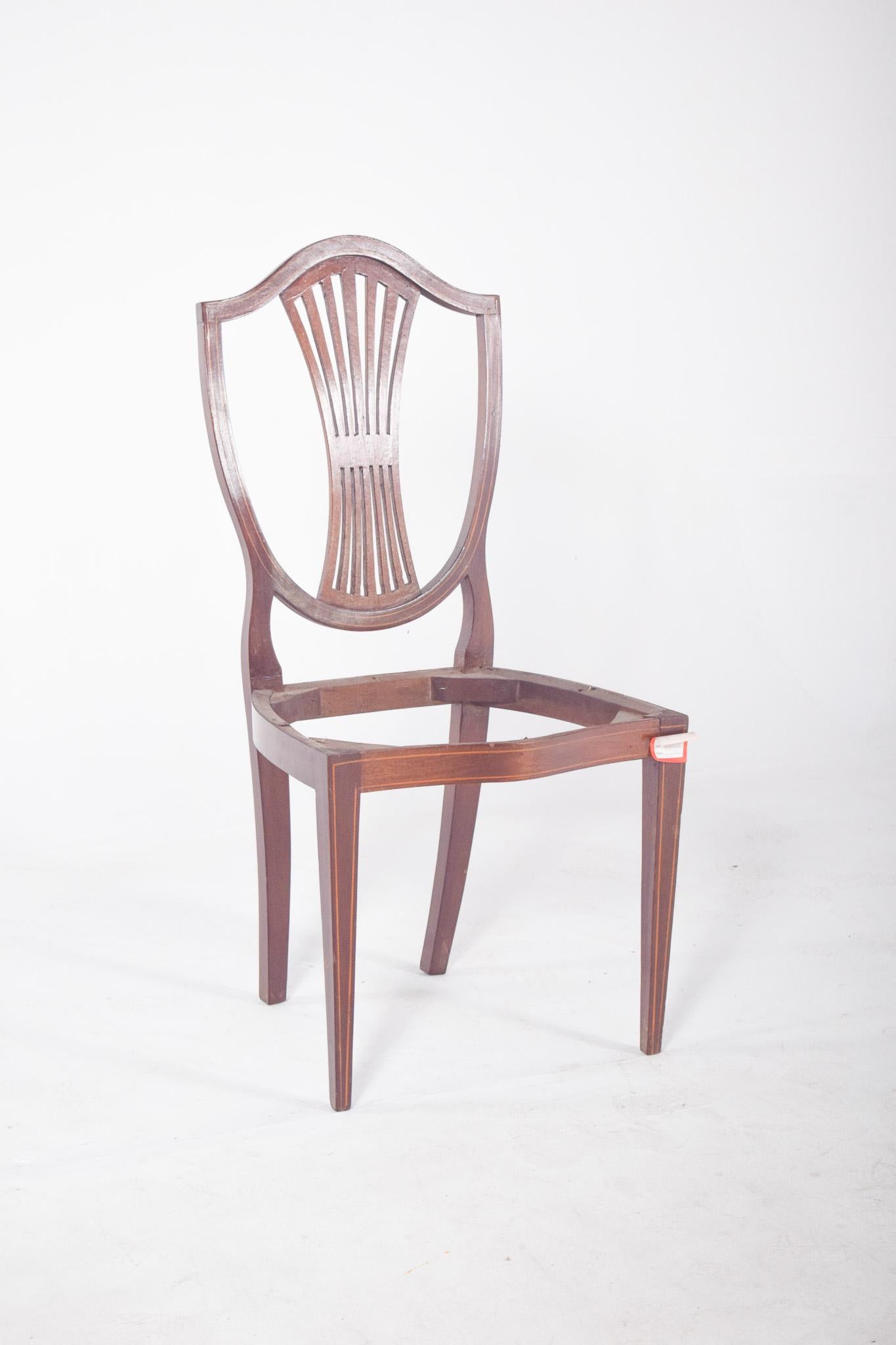 Silla de estilo Hepplewhite, sin asiento. Con una estructura de madera noble y finas líneas de incrustaciones contrastadas que realzan los contornos del respaldo y las patas. El respaldo tiene una barandilla vertical en forma de abanico con una