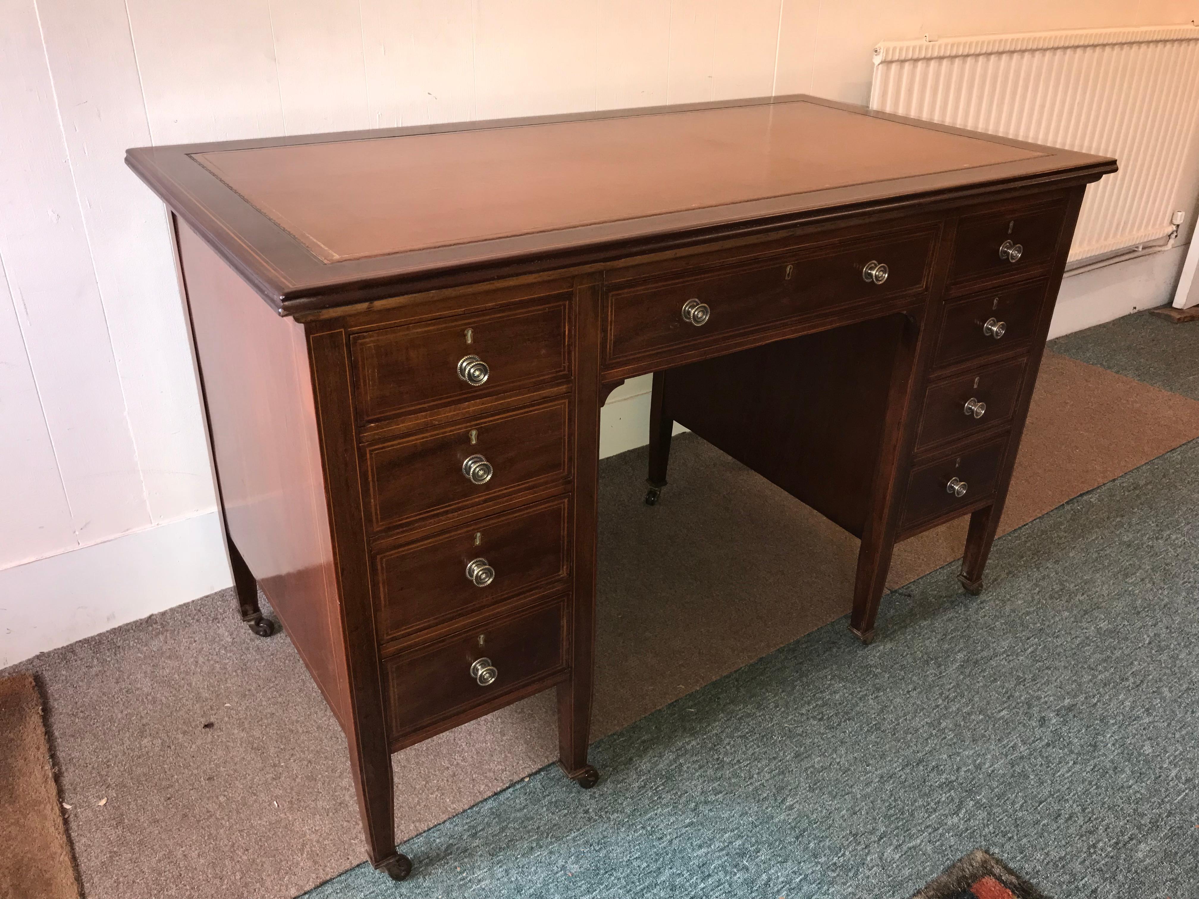 Hepplewhite style mahogany and boxwood inlaid one piece desk with nine deep drawers with brass knobs, ending on square tapered legs. This is a superior quality piece, even the side panels are inlaid. The gilt tooled leather top is in immaculate
