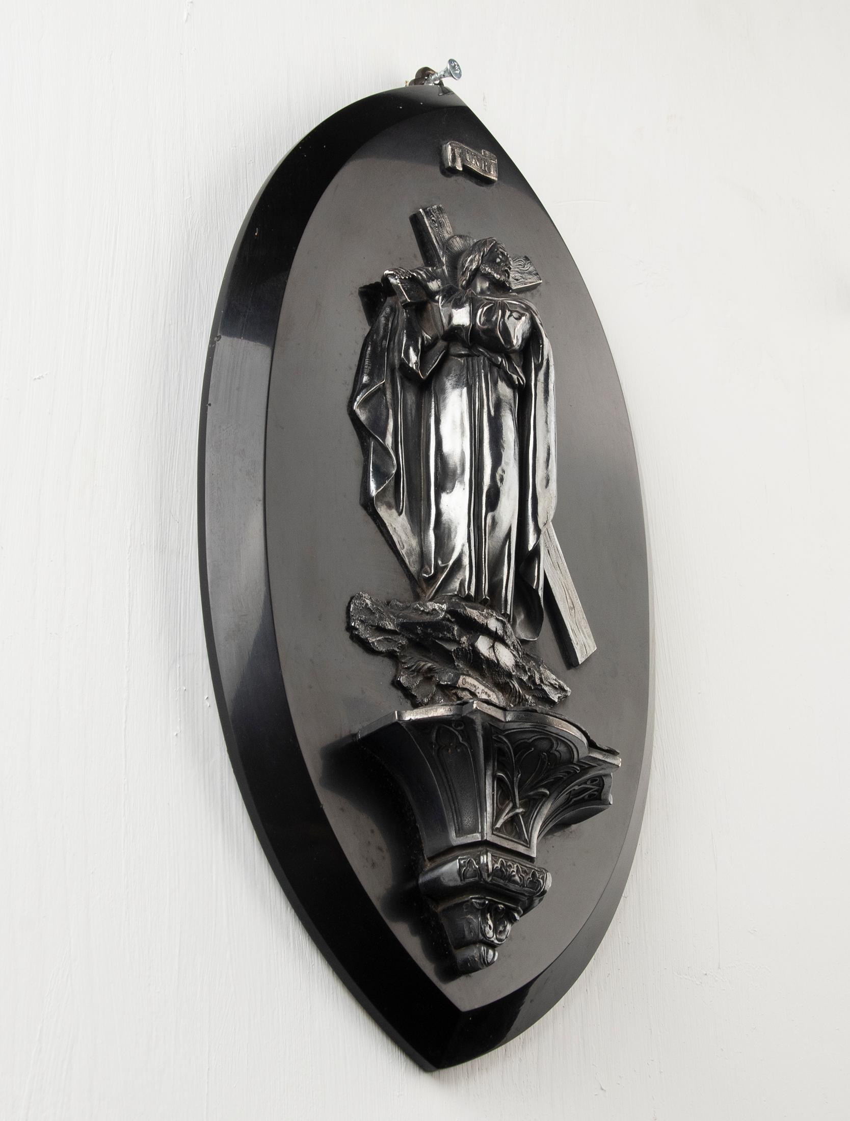 An antique holy water vessel depicting Jesus Christ with the cross on his shoulders. The sculpture is made of silver-plated brass, attached on a black marble panel. The holy water font still has a removable bowl. At the back is a sturdy ring also to