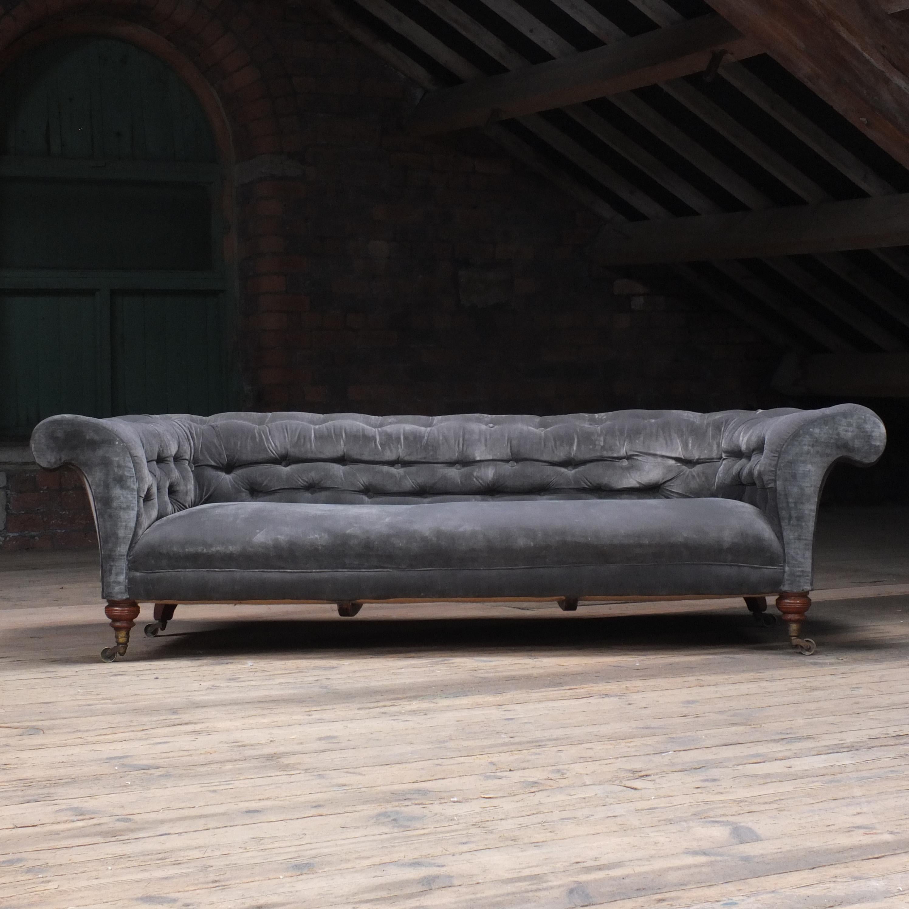 A Large country house English chesterfield sofa by Howard & sons - London. Raised on Howard's uniquely ring turned walnut legs to the front and out swept to the back, all on Howard & son's stamped castors. The low sleek design of Howard
