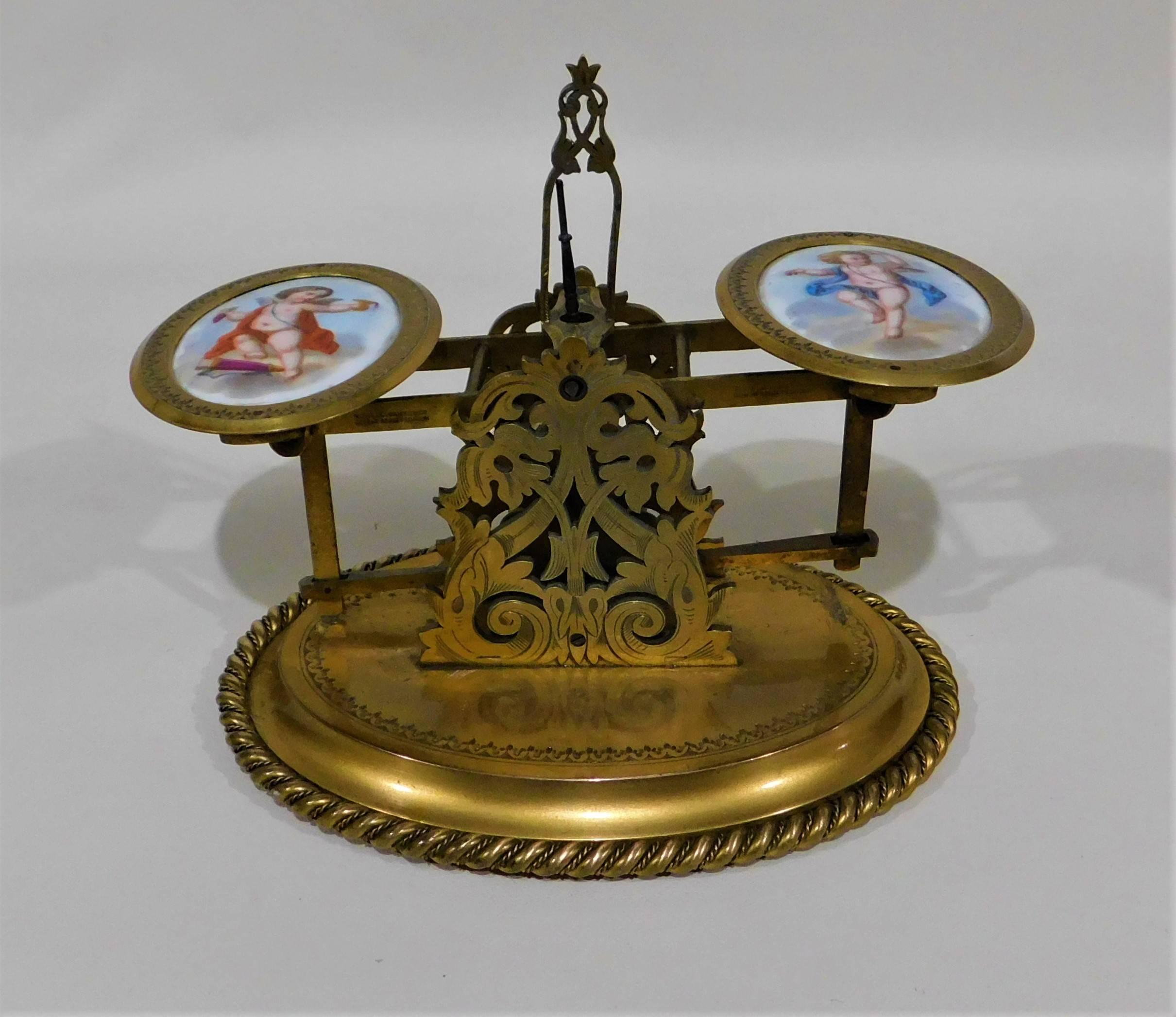 Howell James & Company brass and porcelain postal letter scale, Regent St. London, circa 1880.
With two hand-painted porcelain plaques depicting cherubs and two stacking weights, one ounce and one quarter ounce.

Howell James & Company were a