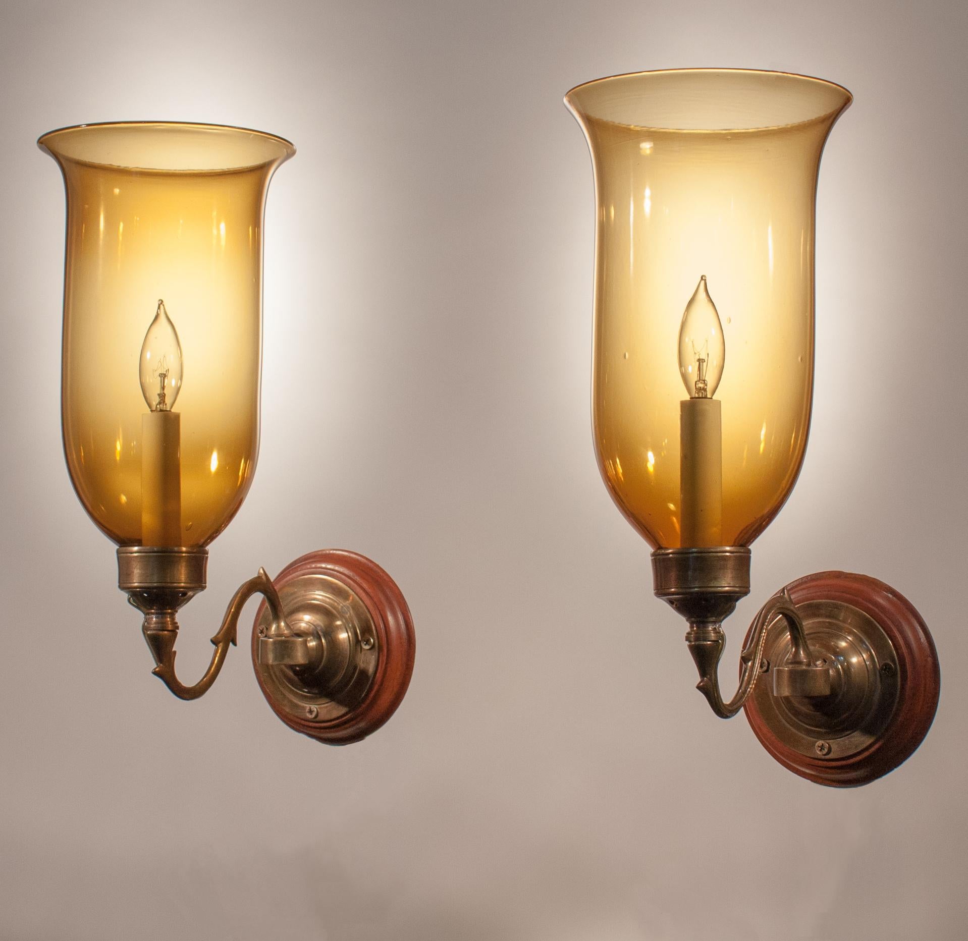 A beautiful pair of English hurricane shades with excellent quality amber-colored handblown glass in a flared form. Originally for candles, these wall sconces have been newly electrified, each with a single candelabra bulb. Custom-fabricated brass